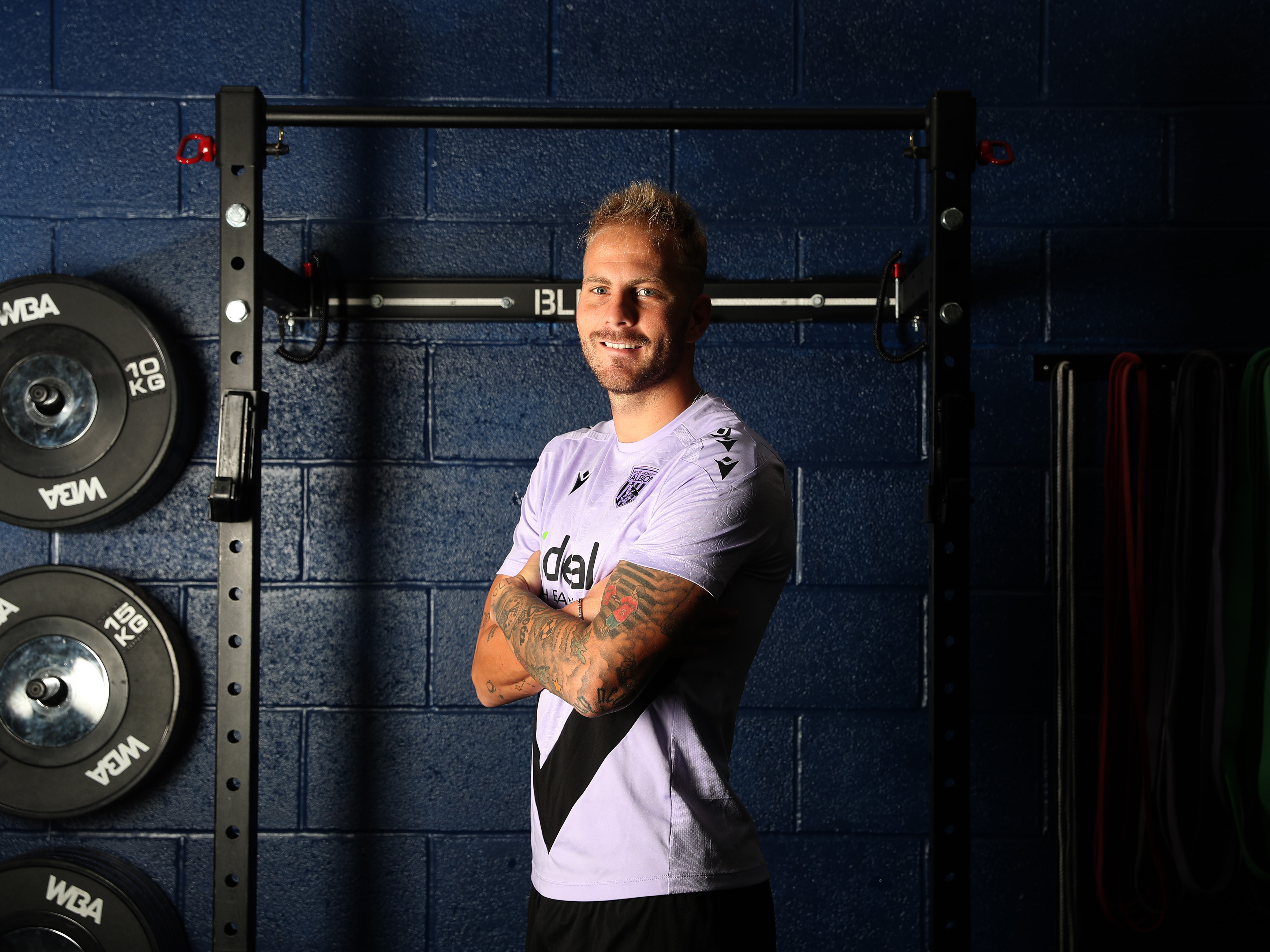 Uroš Račić smiling at the camera while stood in the gym with his arms folded 