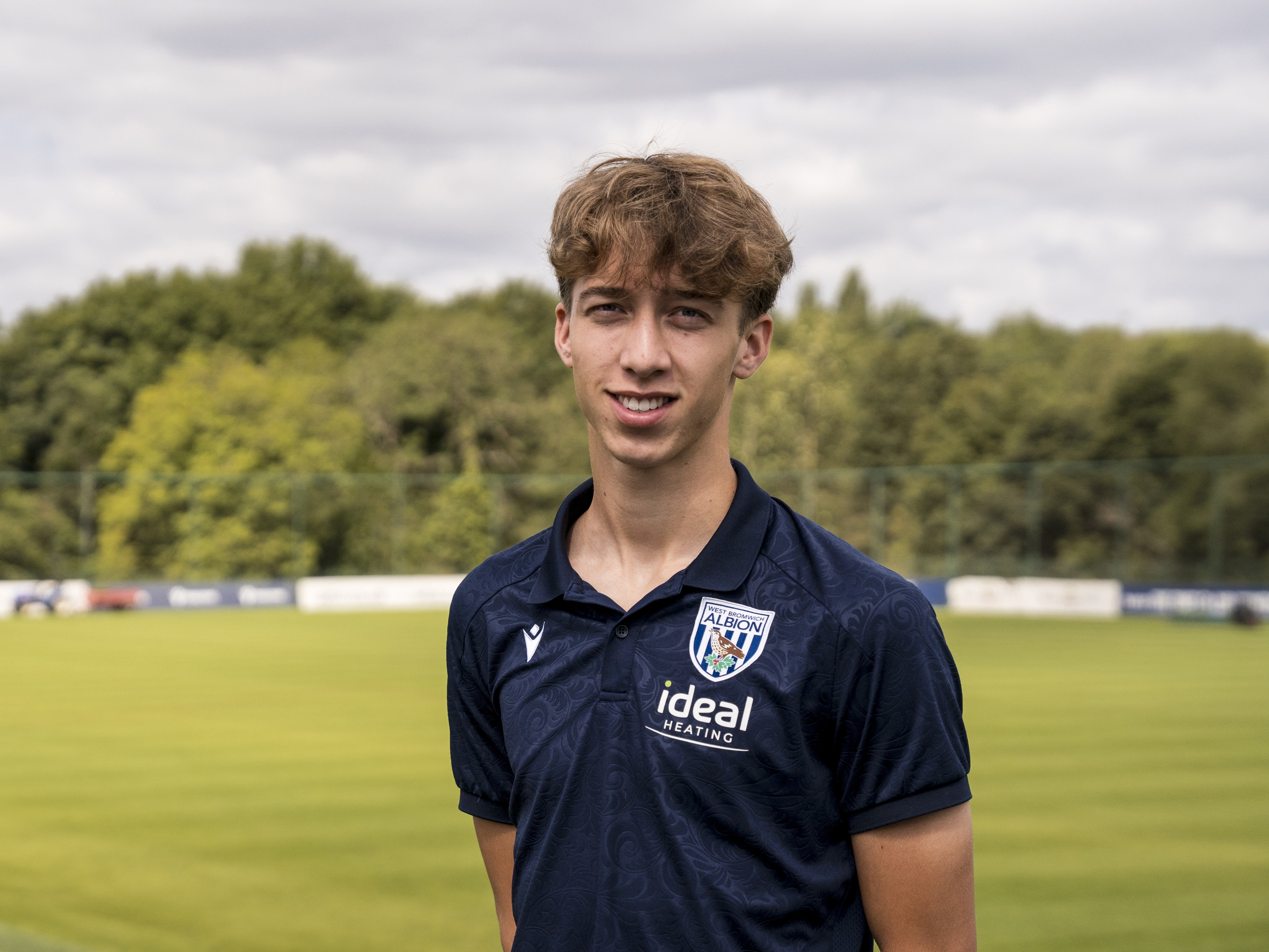 Harry Whitwell smiling at the camera with a training pitch in the background 