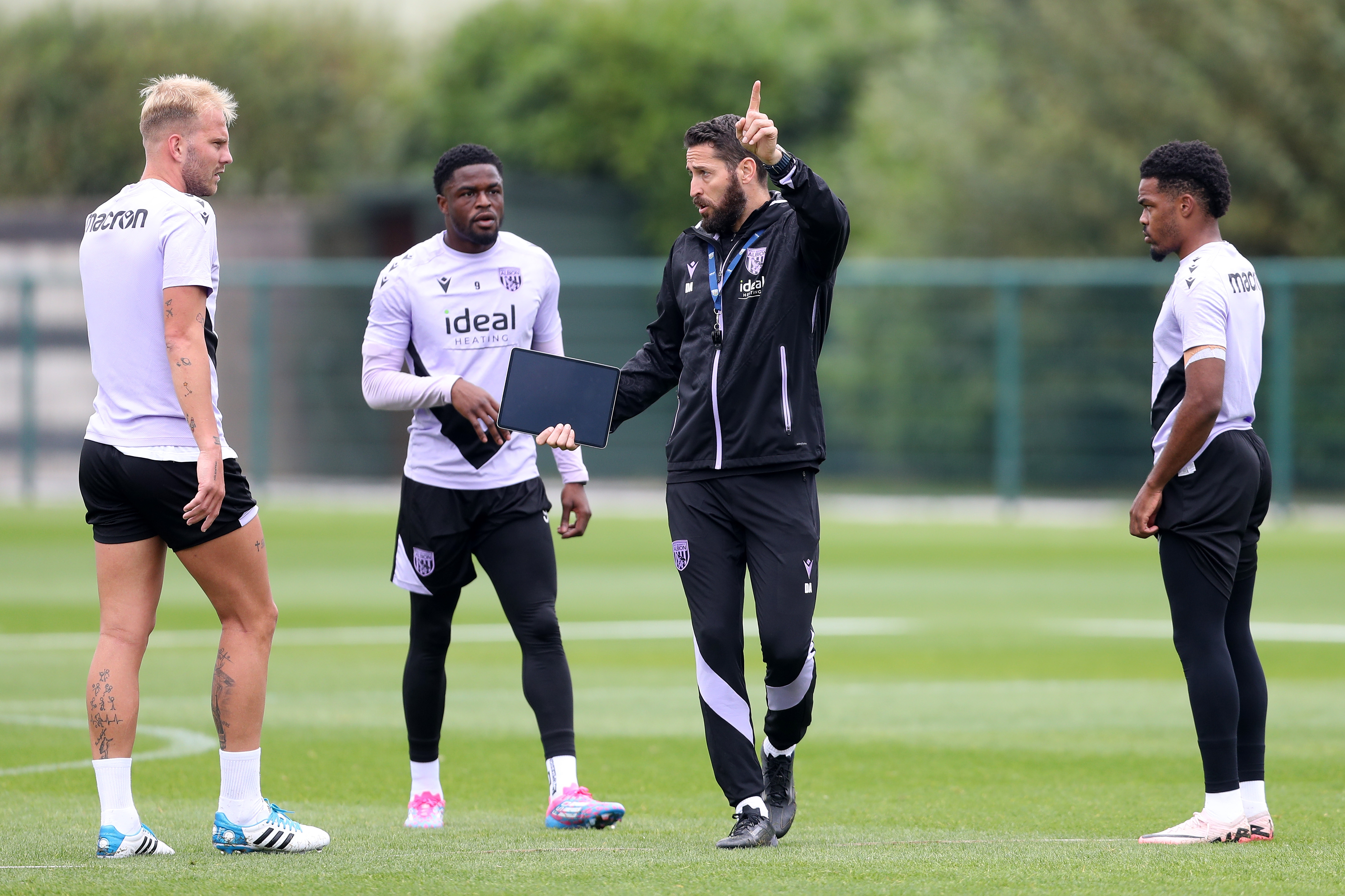 Coach Damia Abella delivering instructions to three players on the training pitch