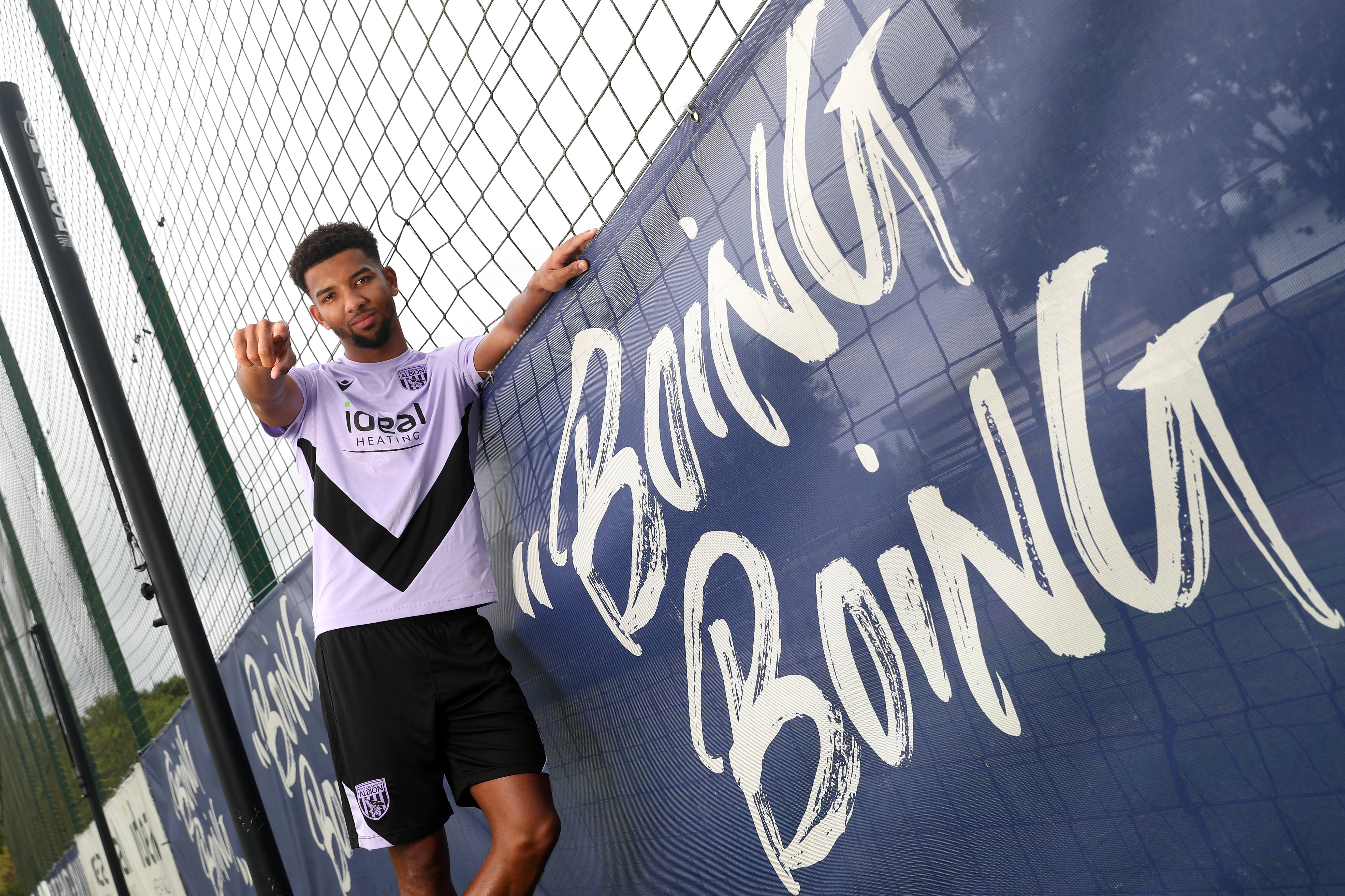 Mason Holgate stood in the home shirt next to a sign which says Boing Boing pointing and smiling at the camera  