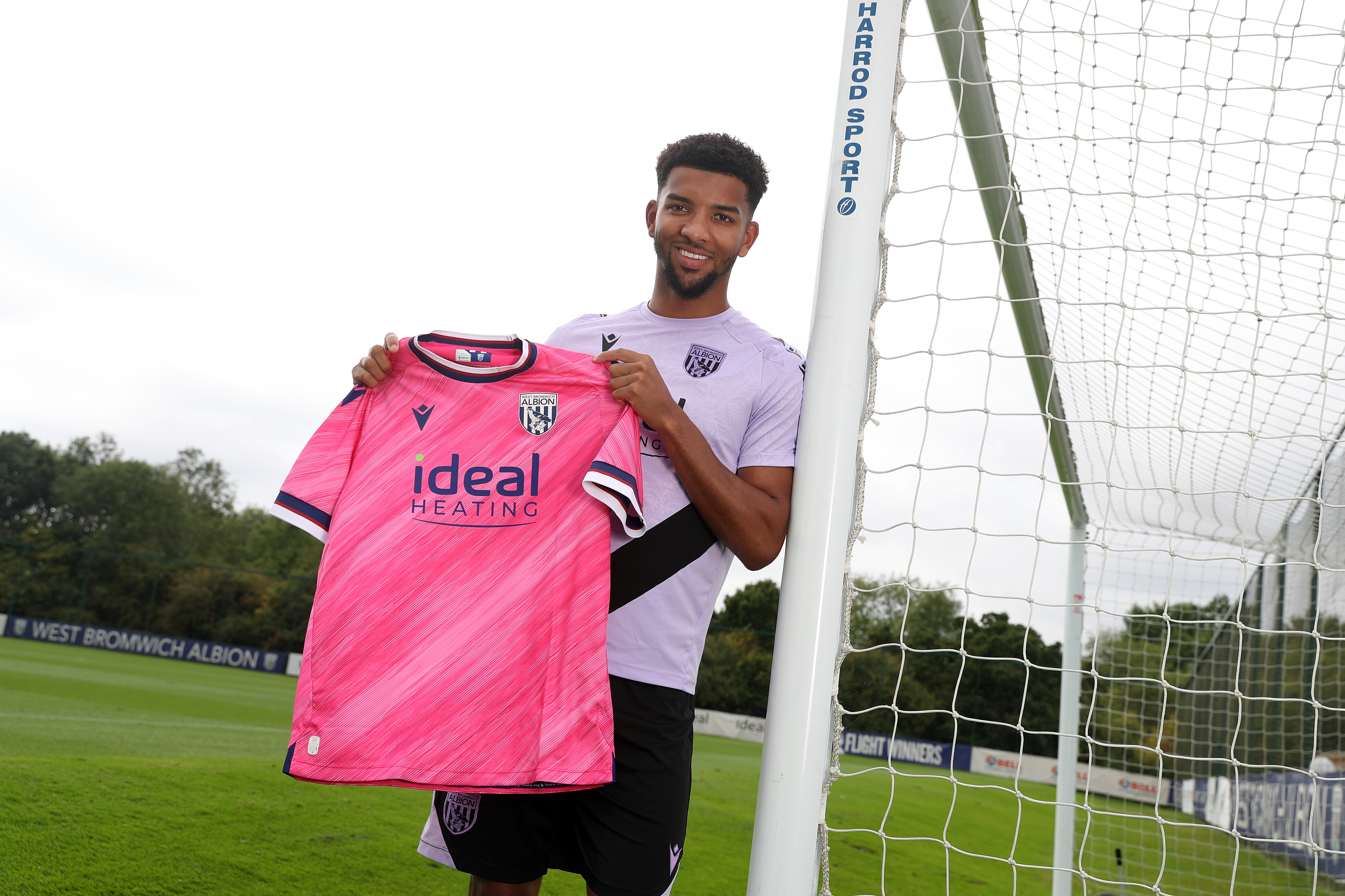 Mason Holgate smiling at the camera holding up a pink away shirt 