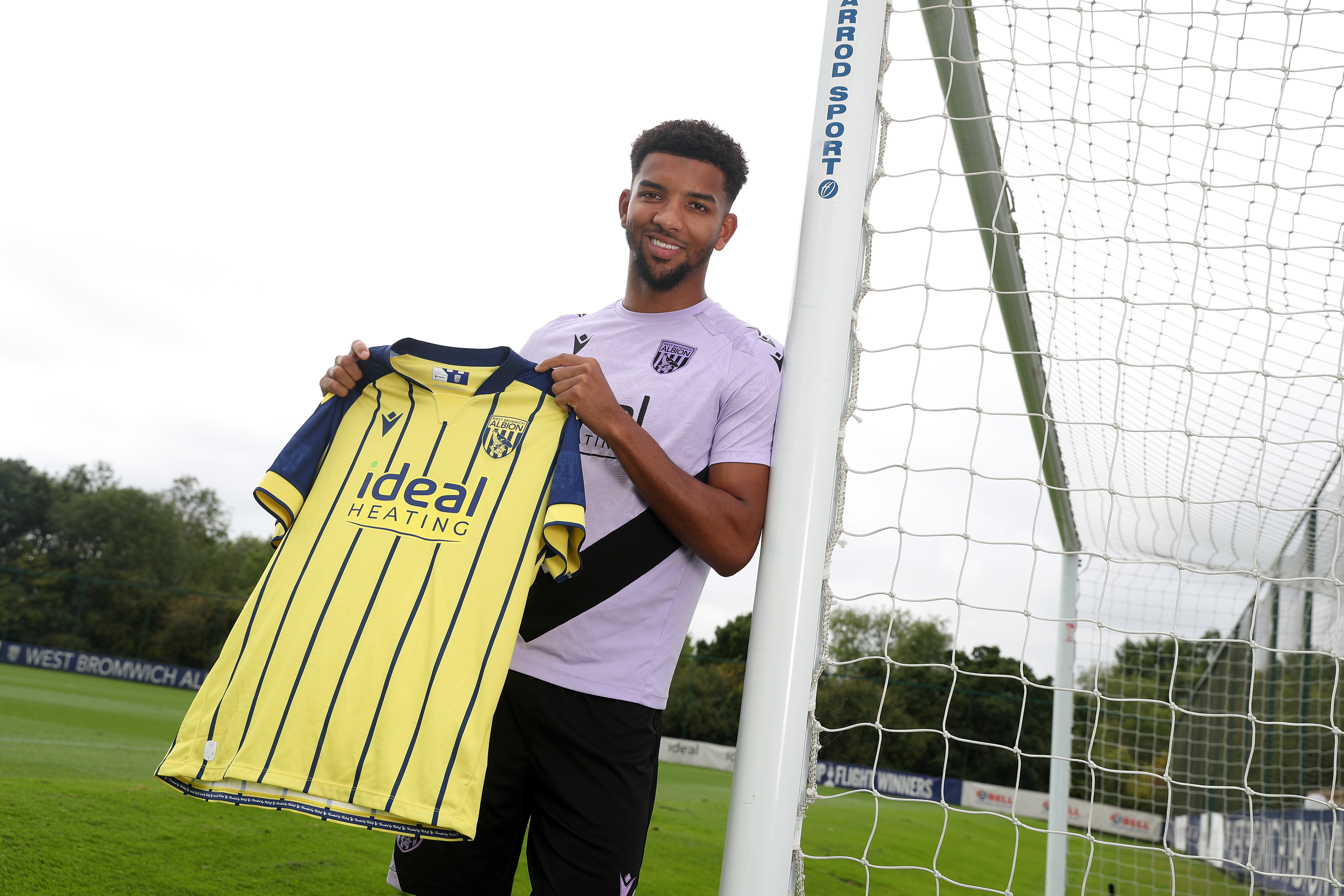 Mason Holgate smiling at the camera holding up a yellow away shirt 