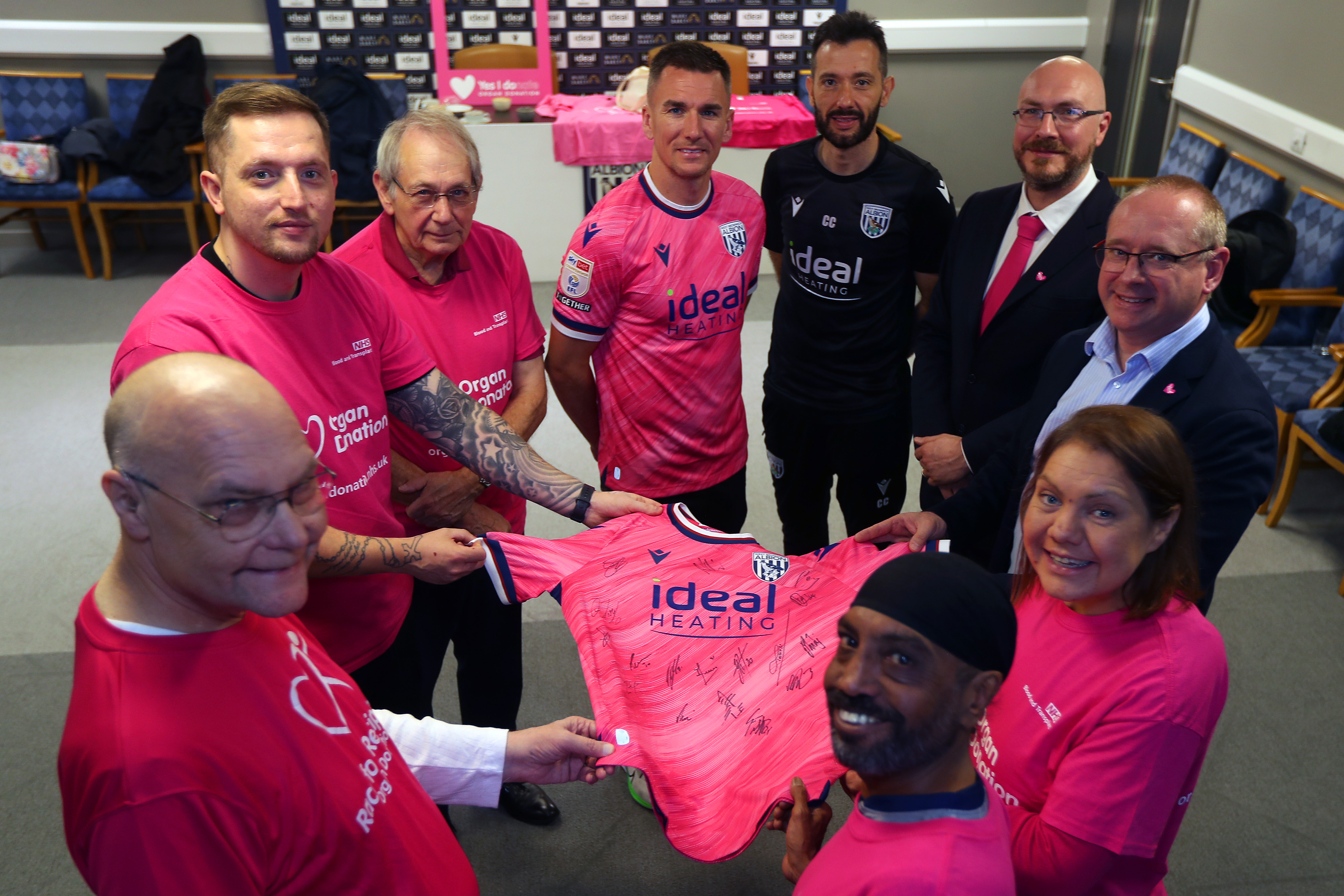 Carlos Corberán and Jed Wallace hold a pink Albion shirt up with several members of the Birmingham Adult Transplant Sport Team