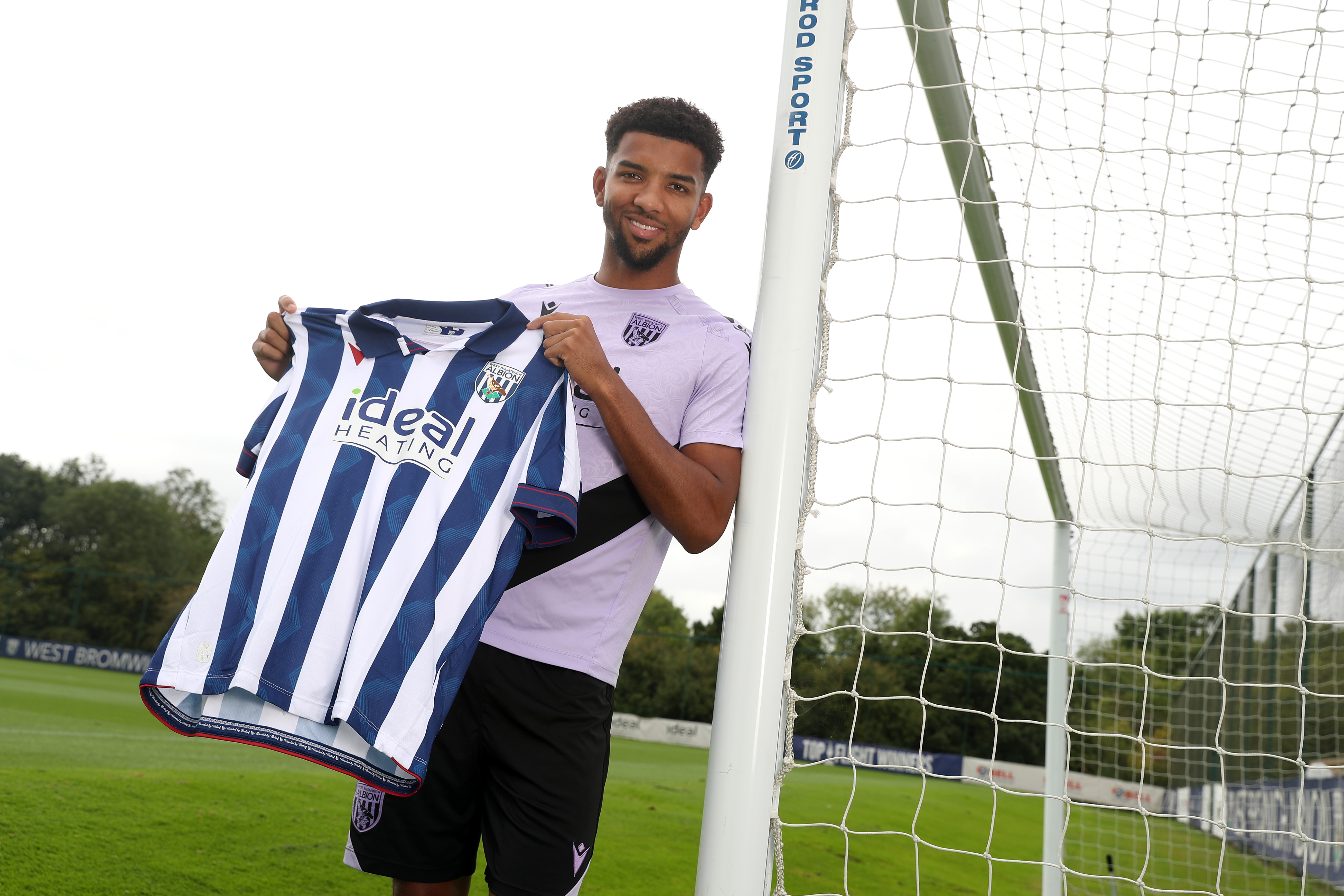 Mason Holgate smiling at the camera while holding up a home shirt stood next to a goal post