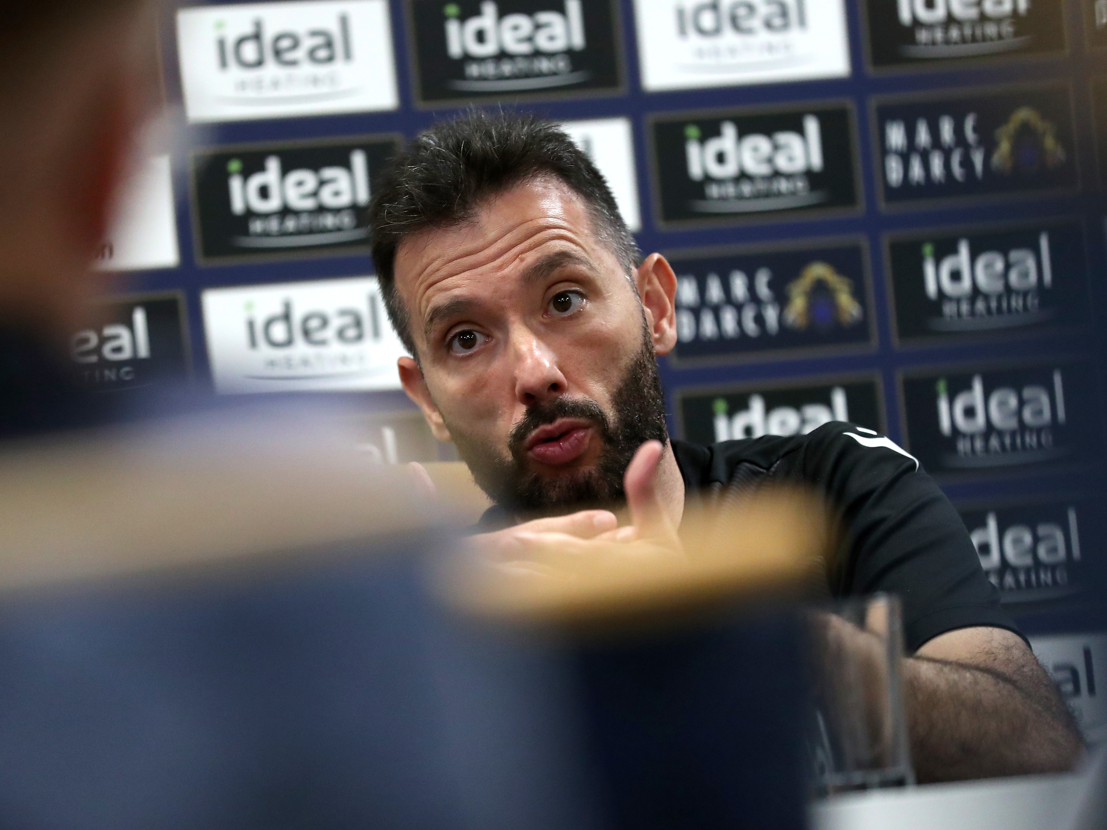 Carlos Corberán sat in a press conference in front of an advertising board 