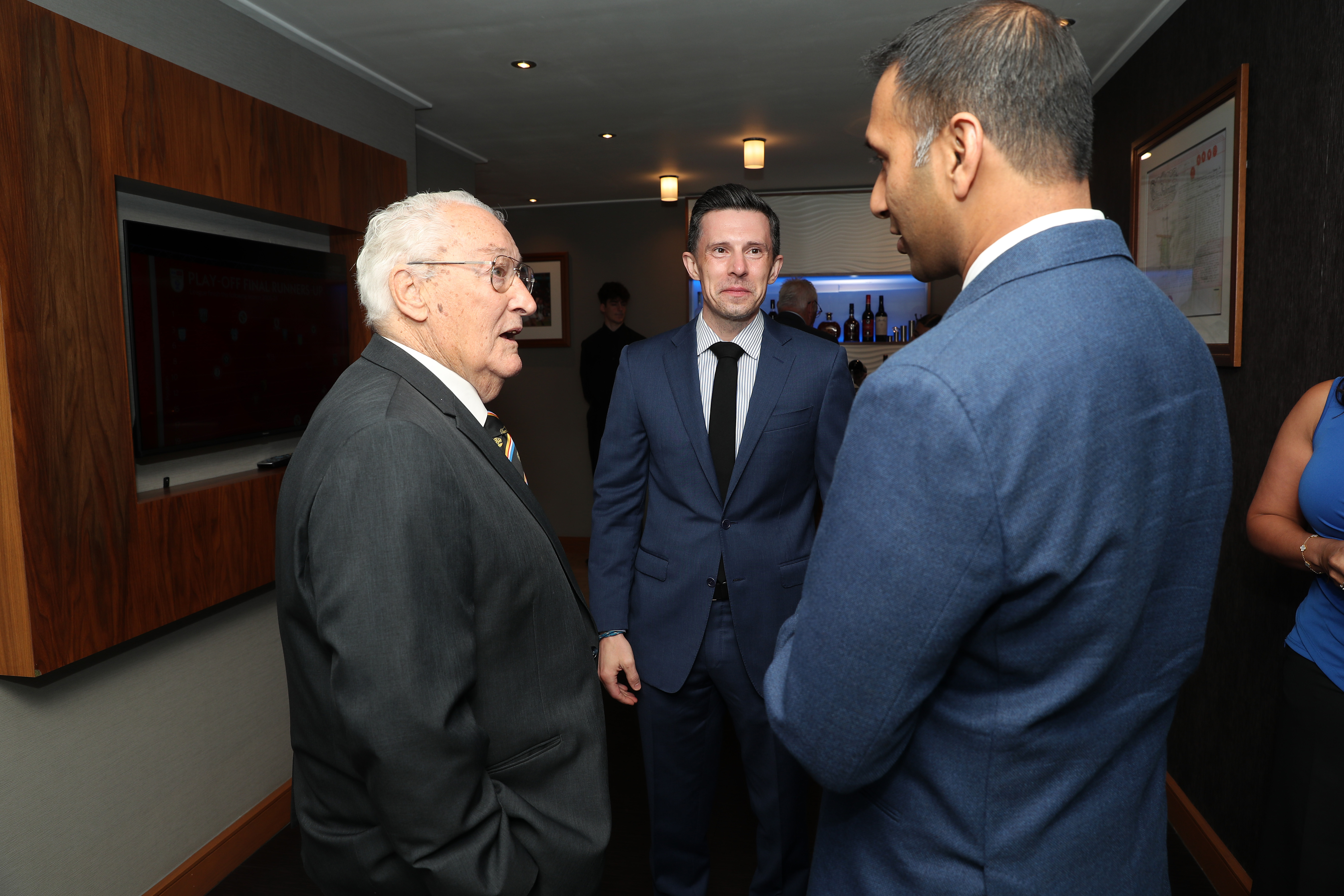 Graham Williams, Andrew Nestor and Shilen Patel chatting in a room all wearing suits 