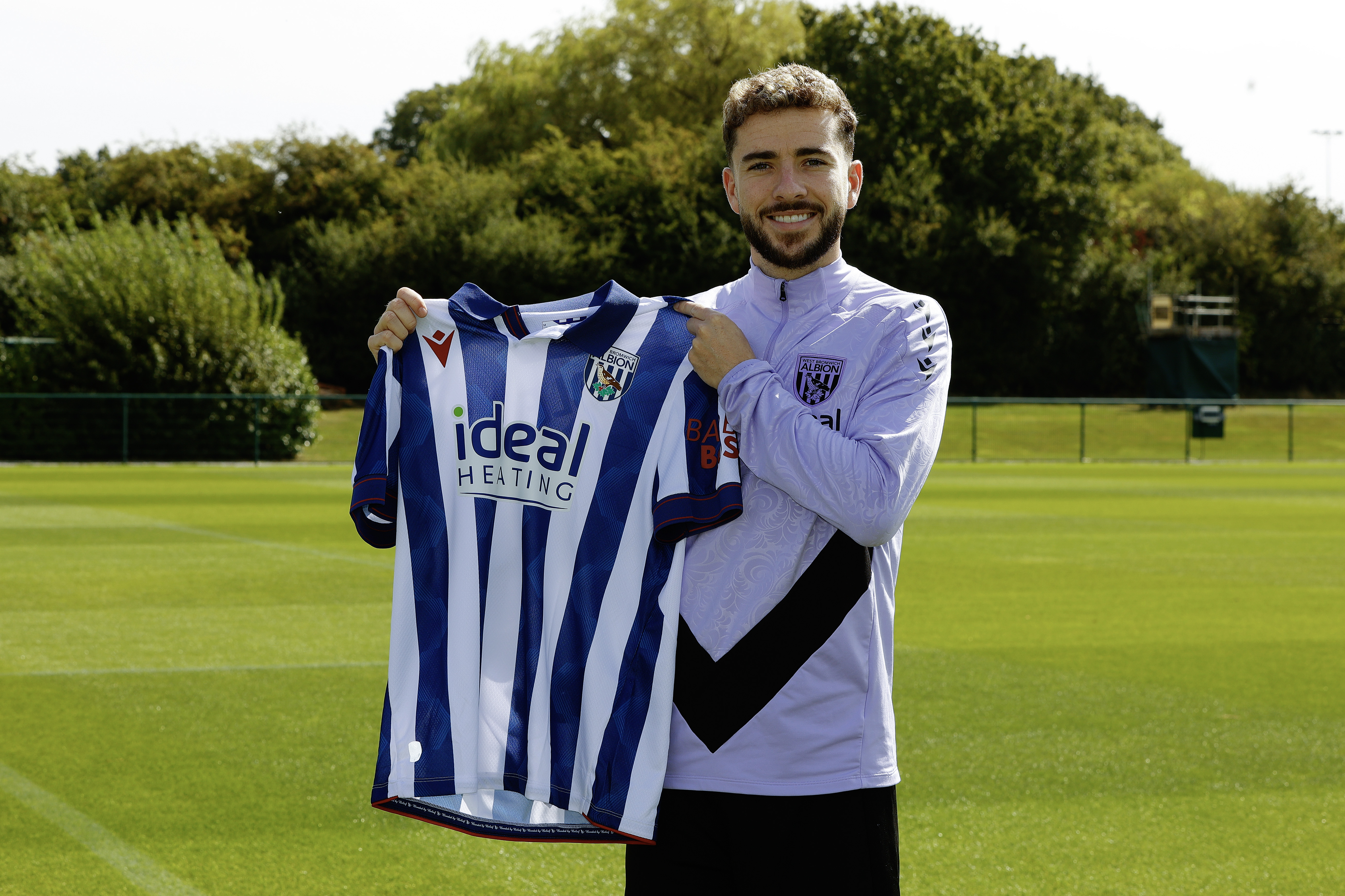 Mikey Johnston smiling at the camera holding up a home Albion shirt