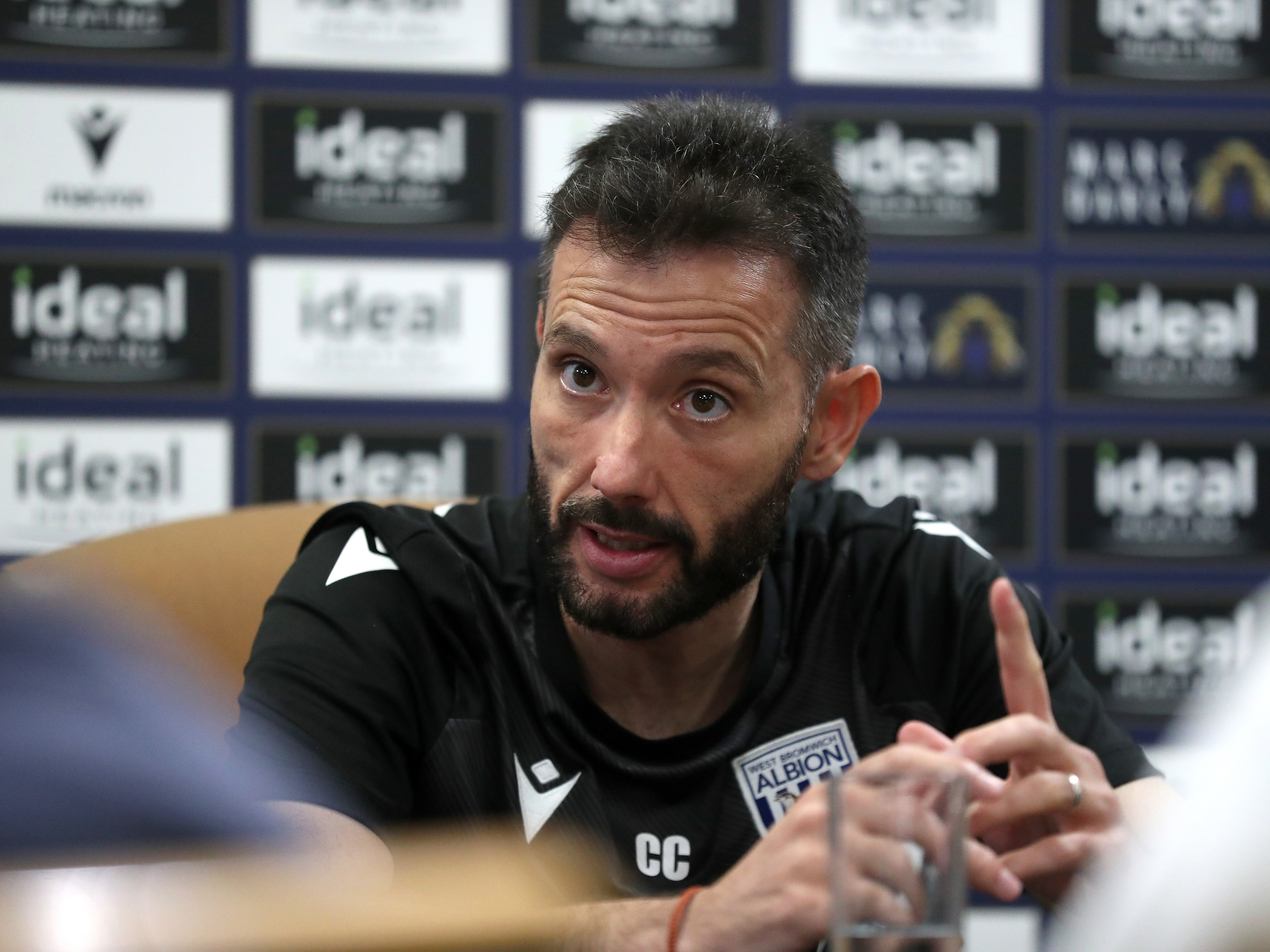 Carlos Corberán speaks to media in front of advertising boards 