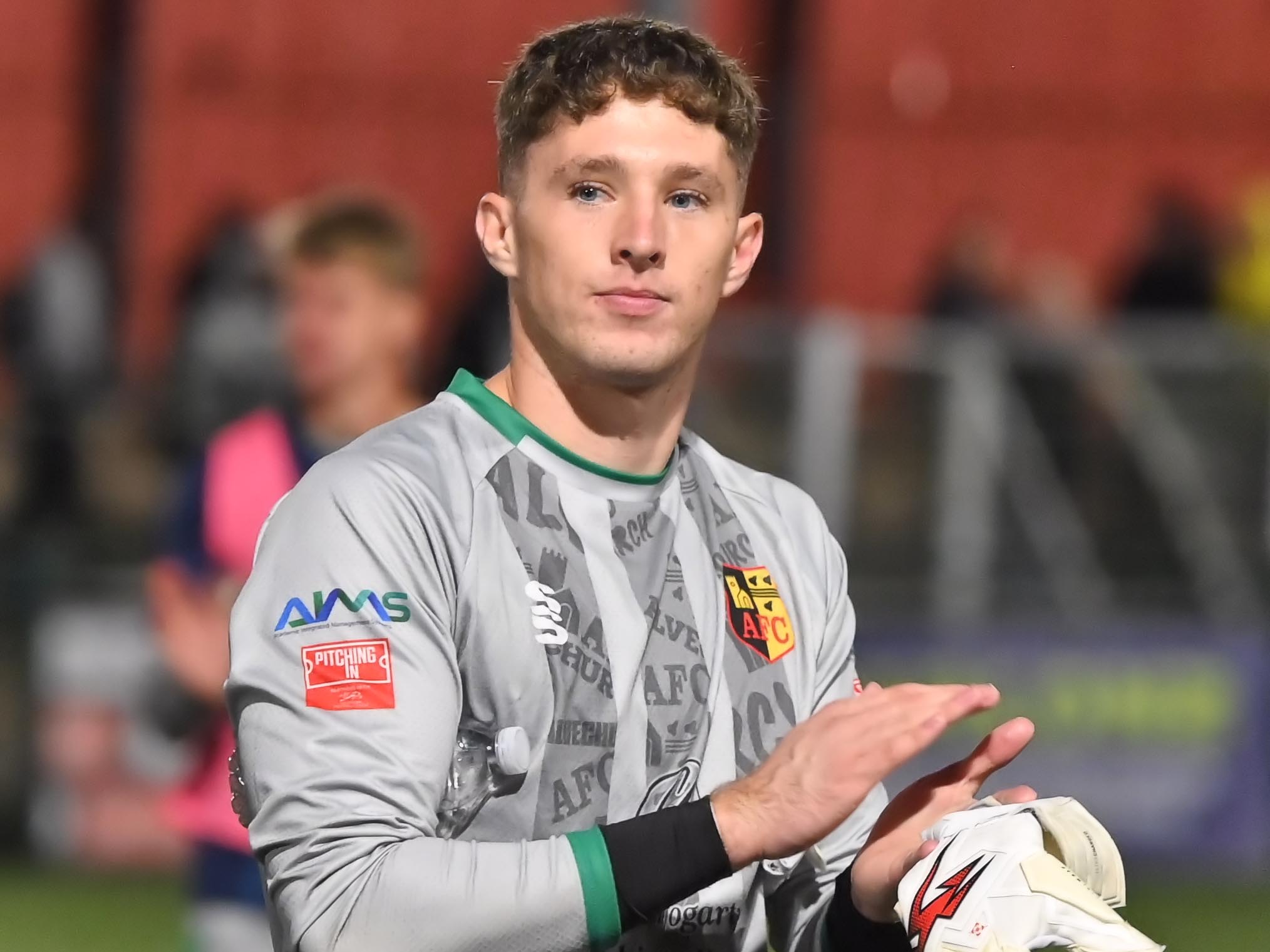 A photo of young shot-stopper Ronnie Hollingshead, in a grey goalkeeper shirt, applauding fans of loan club Alvechurch