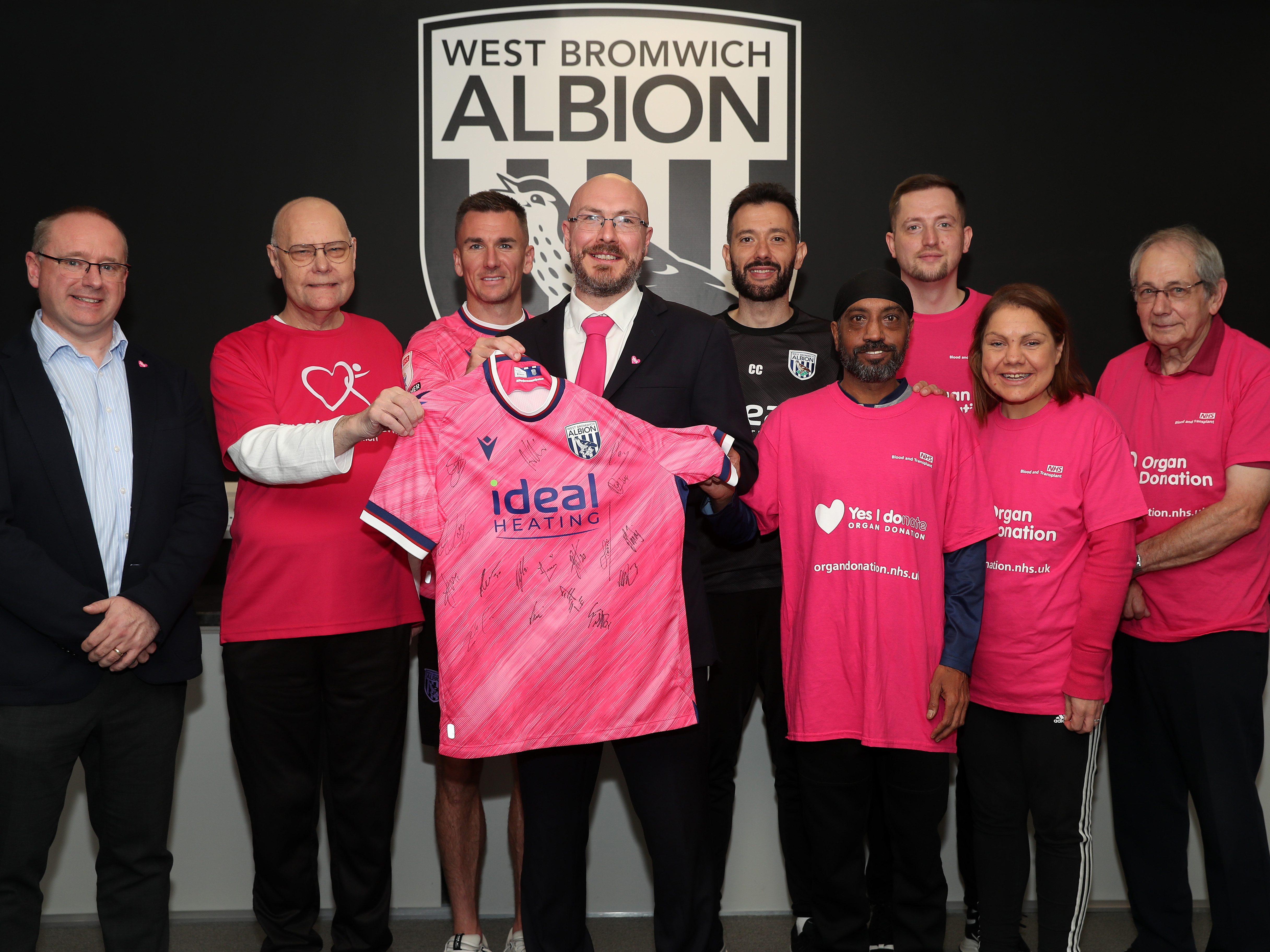 Mark Miles, Carlos Corberán and Jed Wallace pose for a photo with a pink Albion shirt with members of the Birmingham Adult Transplant Sport Team 