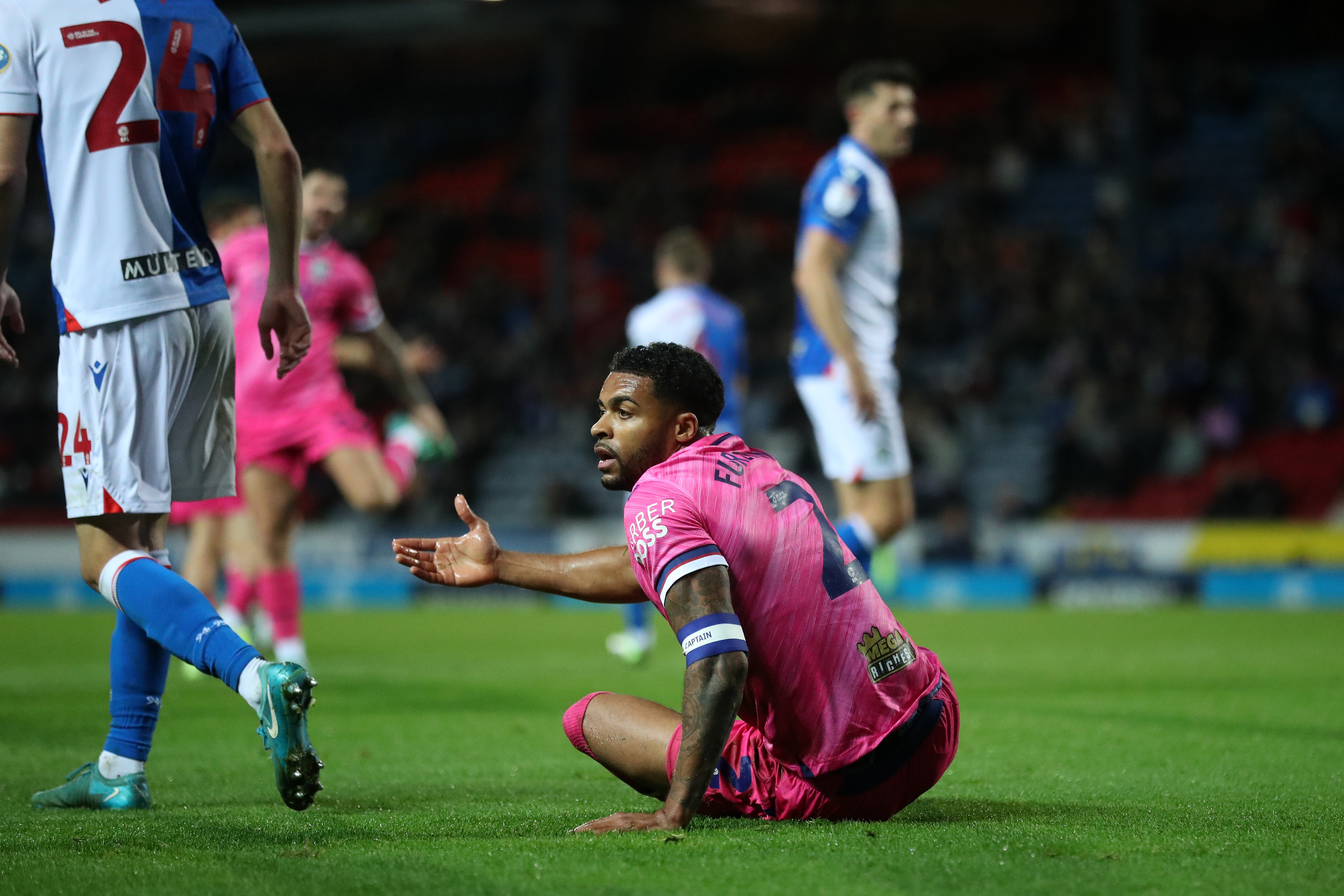 Darnell Furlong sits on the pitch with his arm out at Ewood Park in the pink away kit 