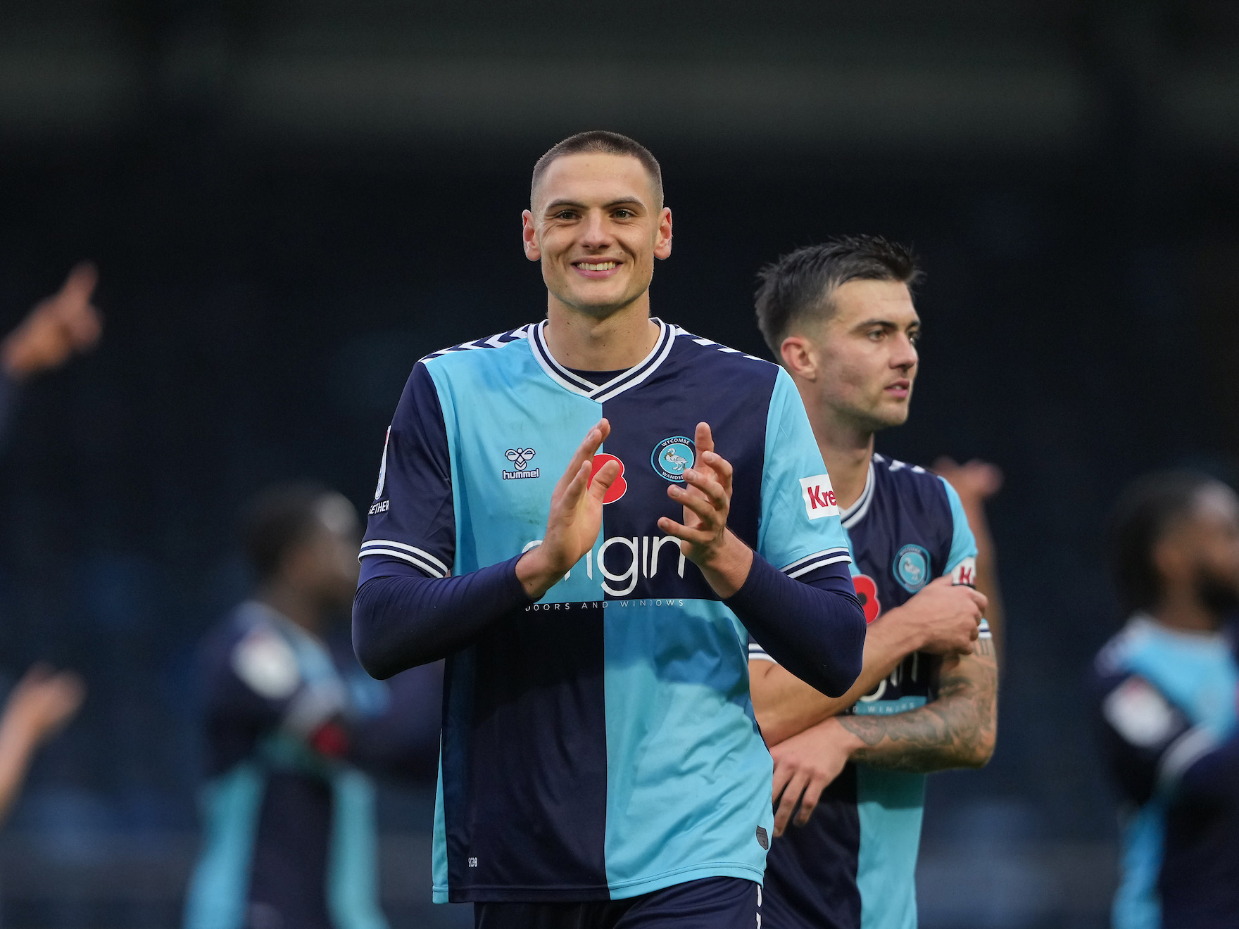 A photo of Caleb Taylor for loan club Wycombe, applauding supporters, wearing their navy and sky blue home kit