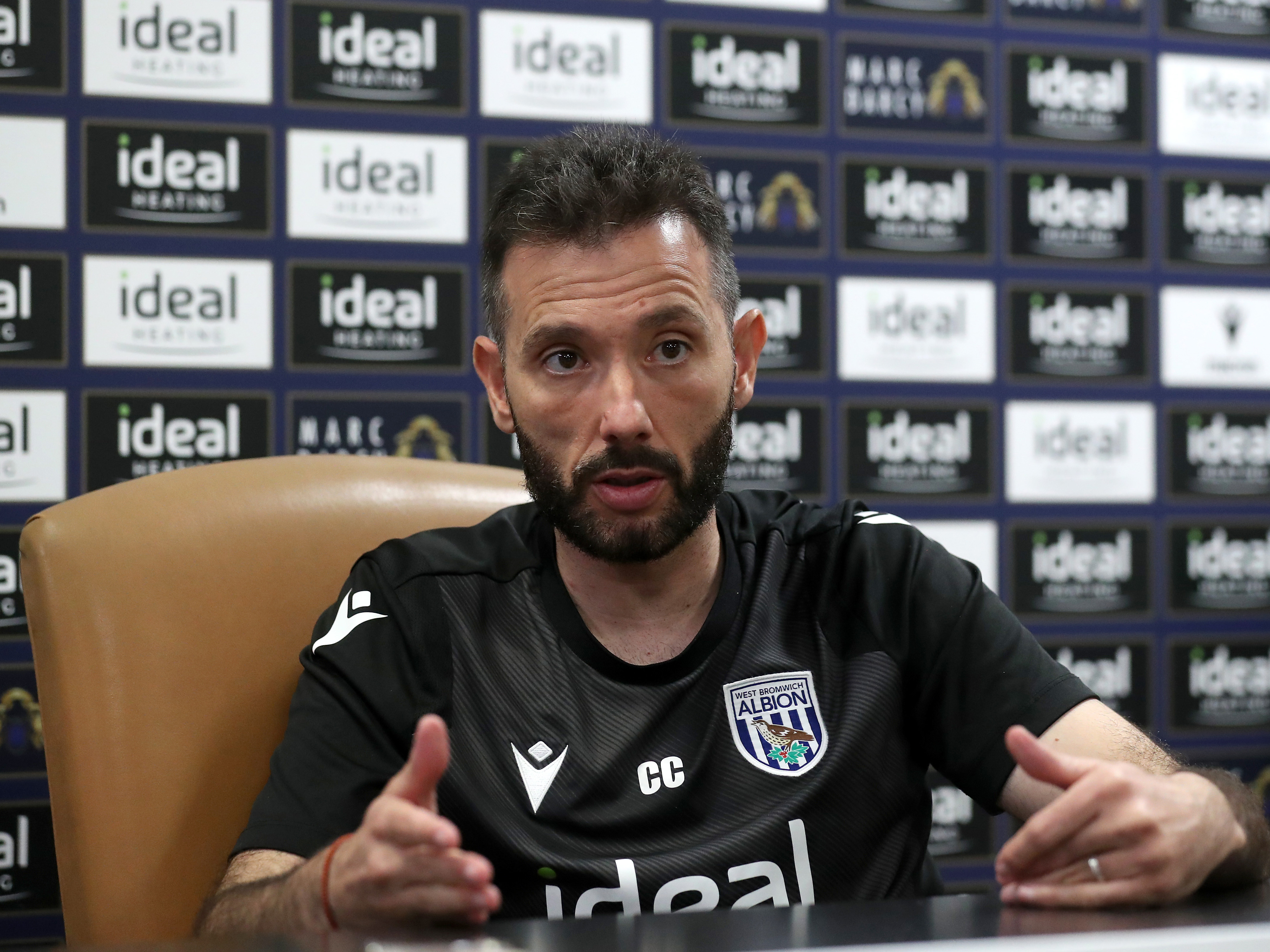 Carlos Corberán speaking to the media in front of advertising boards 