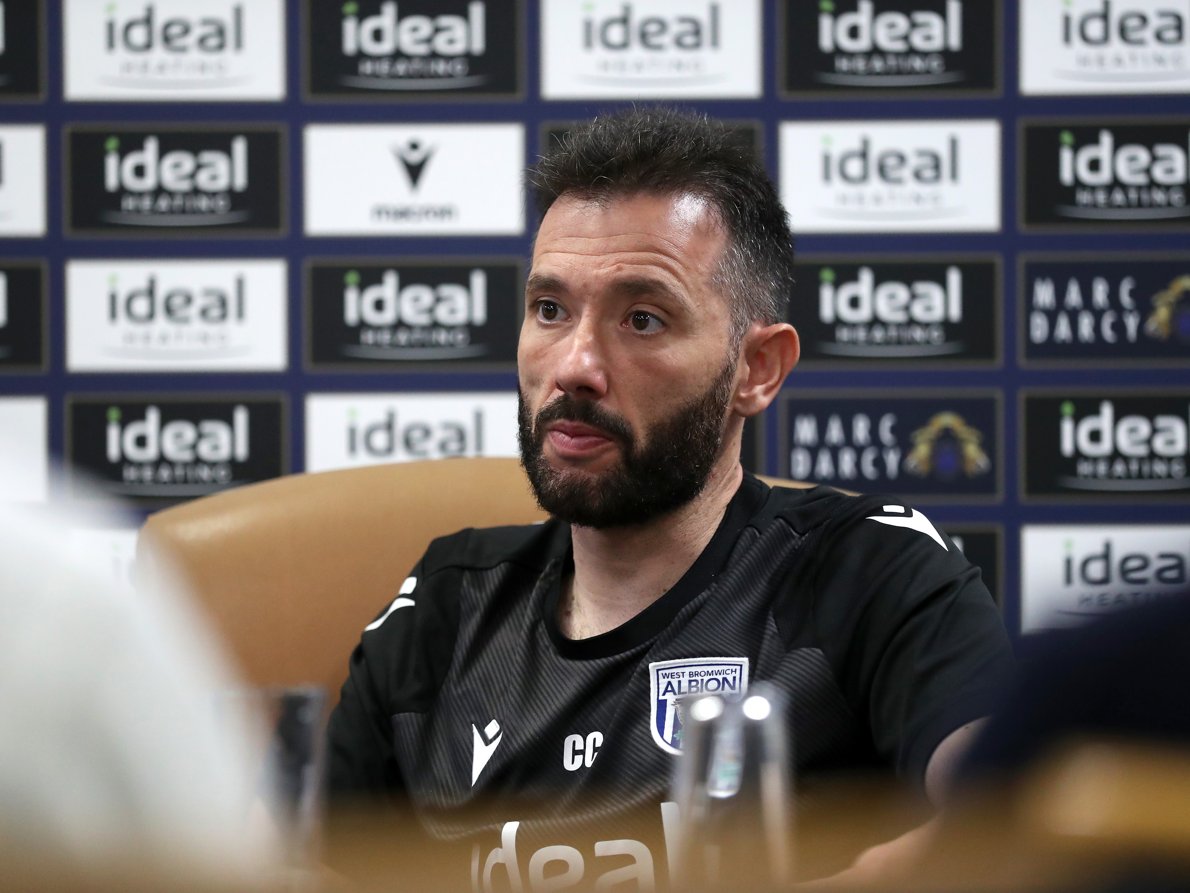 Carlos Corberán speaks to the media in a press conference in front of a press conference board 