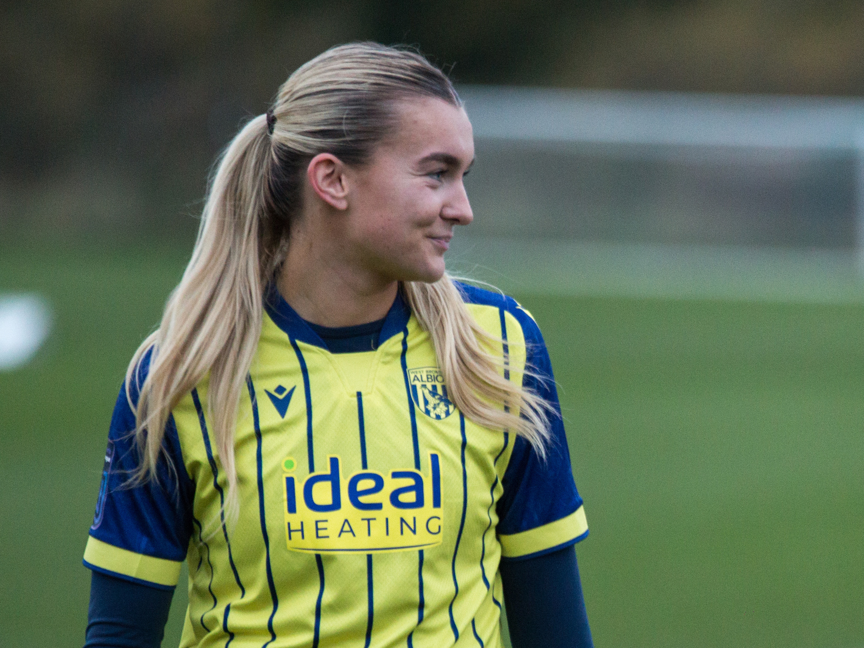 Taylor Reynolds smiling while looking to her left while wearing the yellow away shirt 