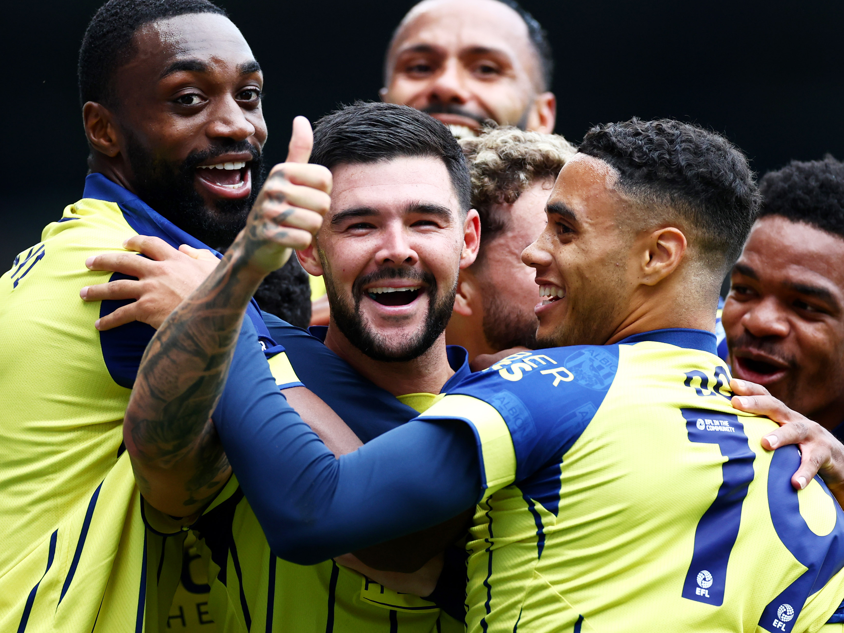 Alex Mowatt celebrates with his thumb up surrounded by team-mates in the yellow away kit at Portsmouth 