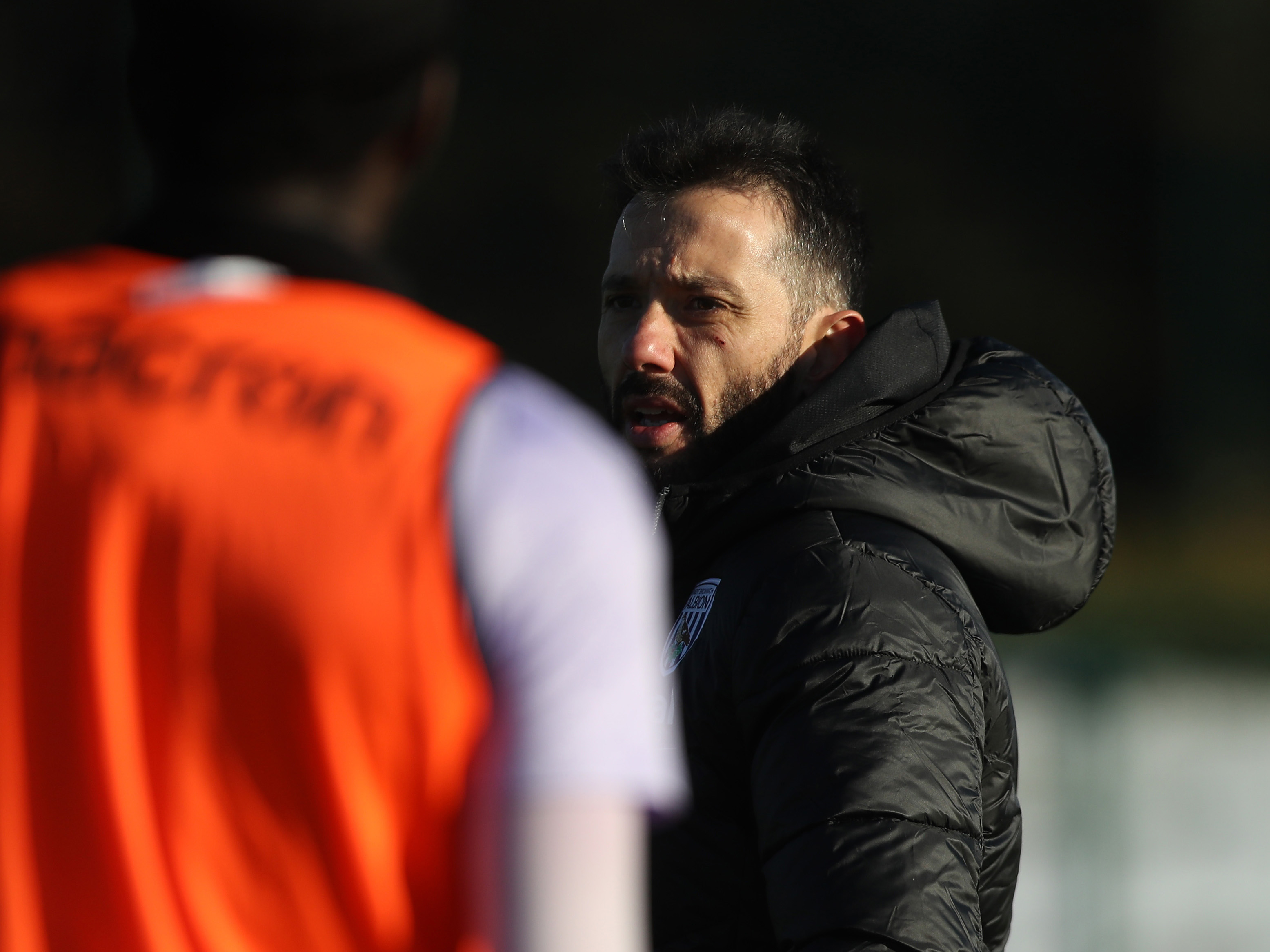 Carlos Corberán watching training while wearing a black coat 