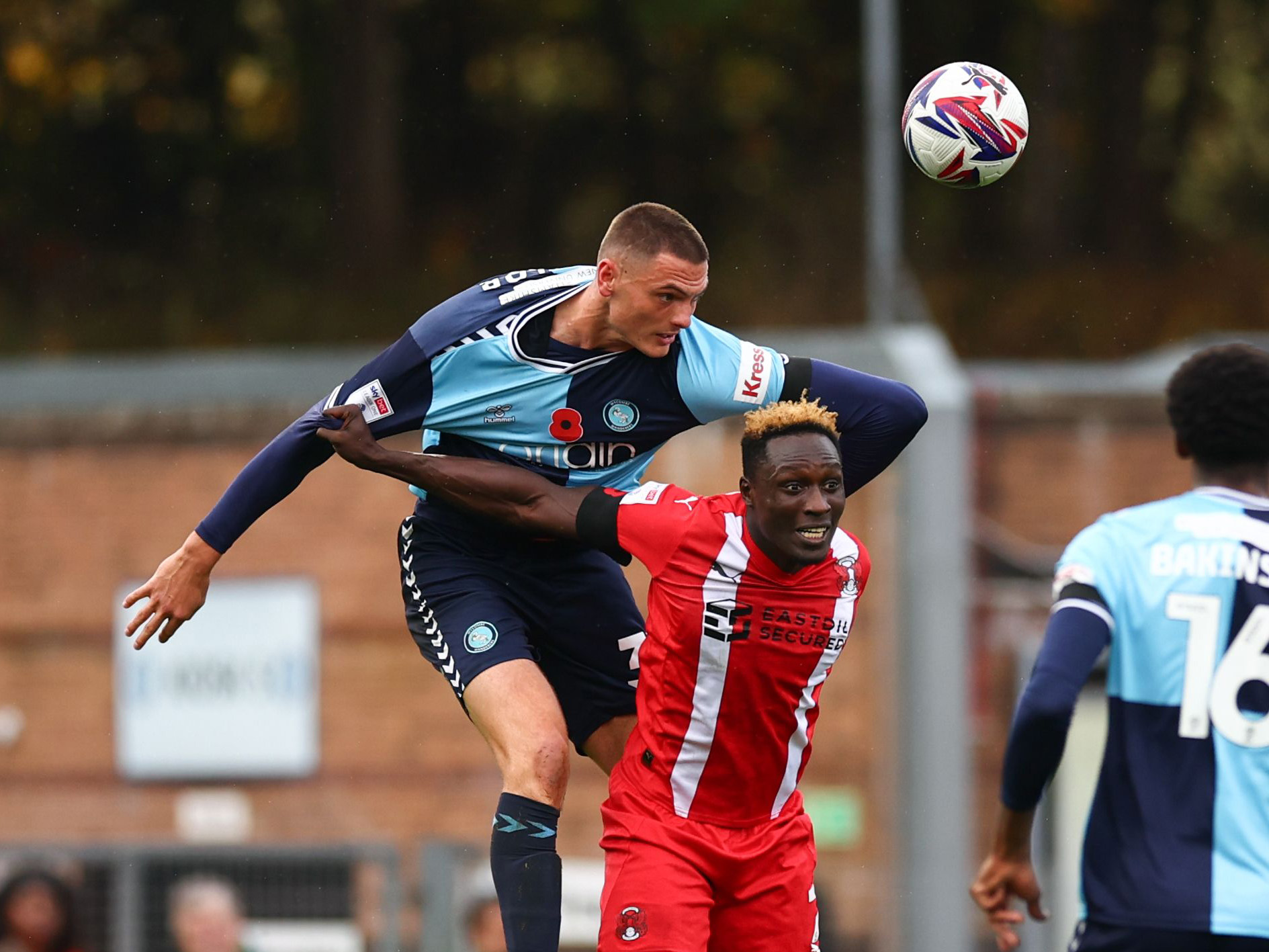 Caleb Taylor jumping to win a header while playing for Wycombe in their home kit 