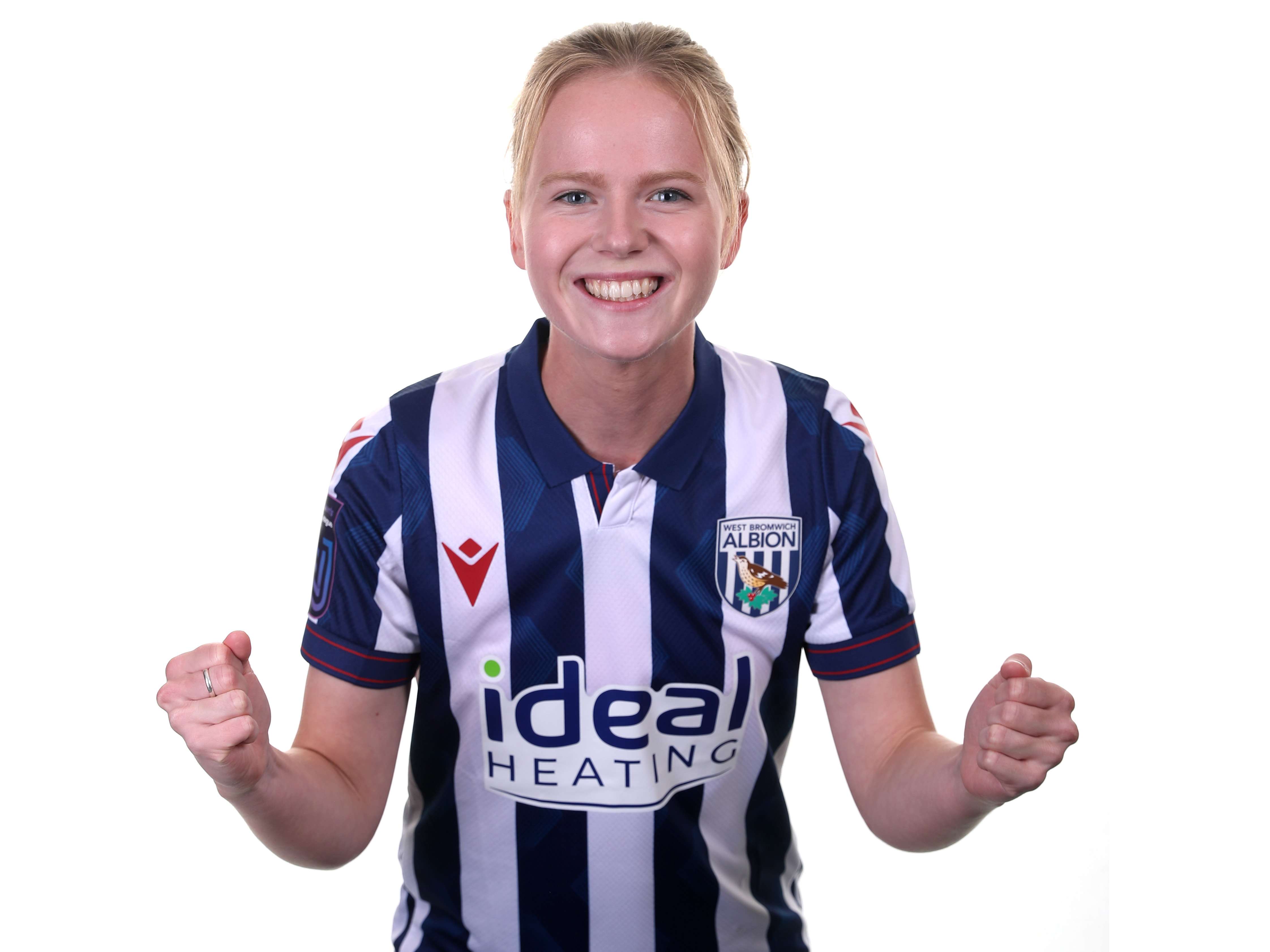 Phoebe Warner pretending to celebrate with her fists clenched while looking at the camera stood in a home shirt 