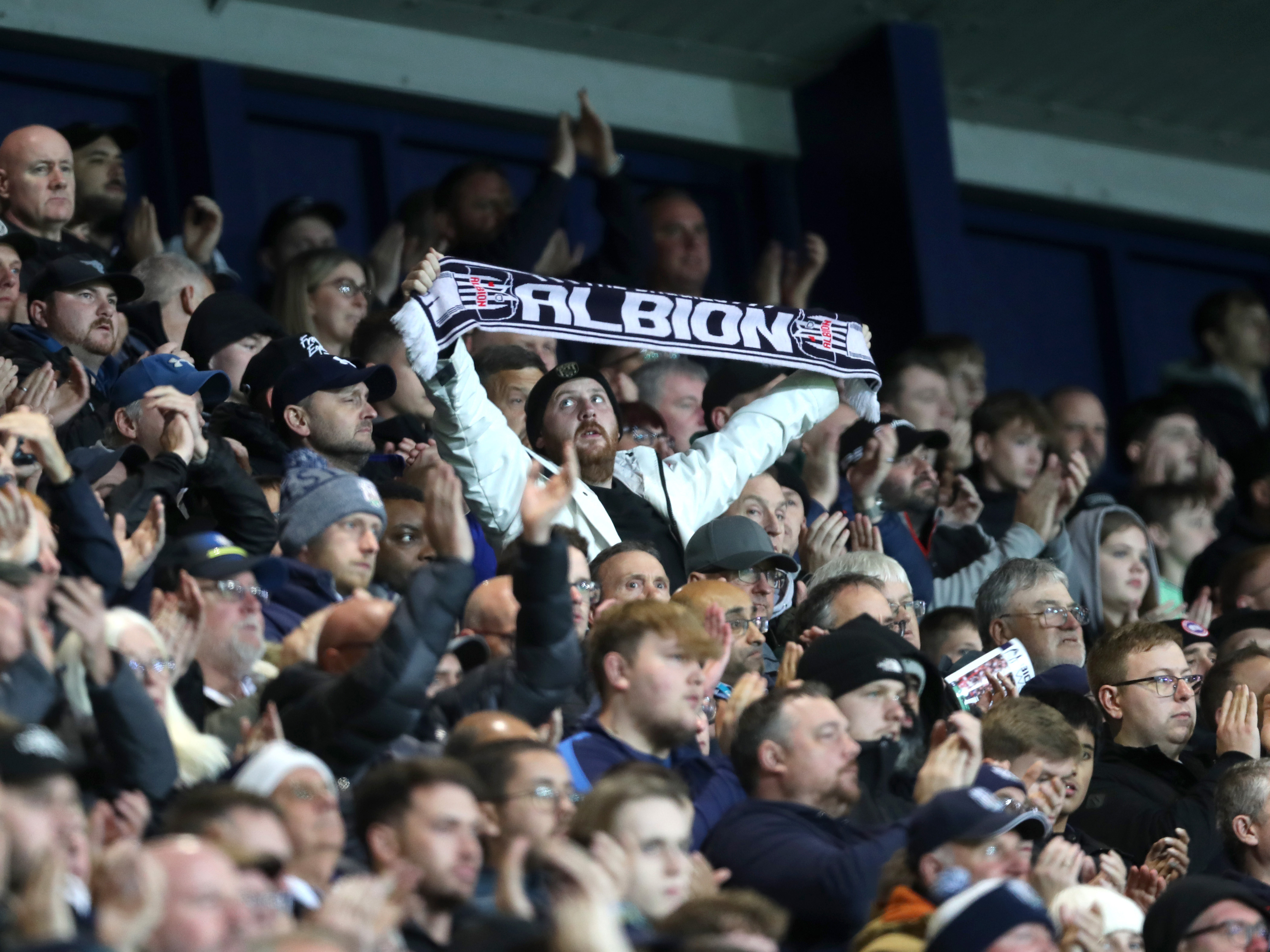 An Albion fan holding up an Albion scarf at a game 