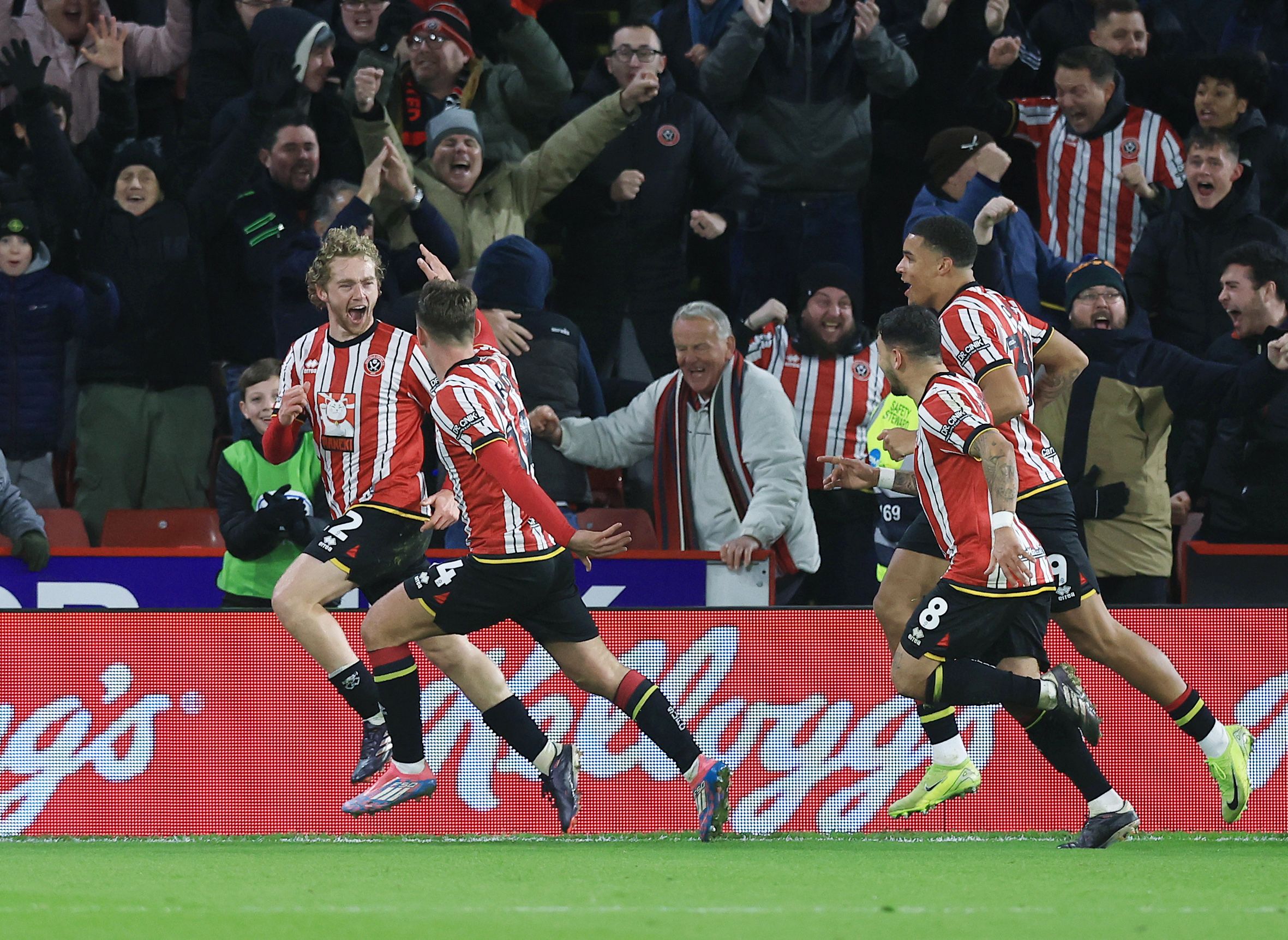 Sheffield United players celebrate a goal scored at home in the home kit with fans celebrating behind them