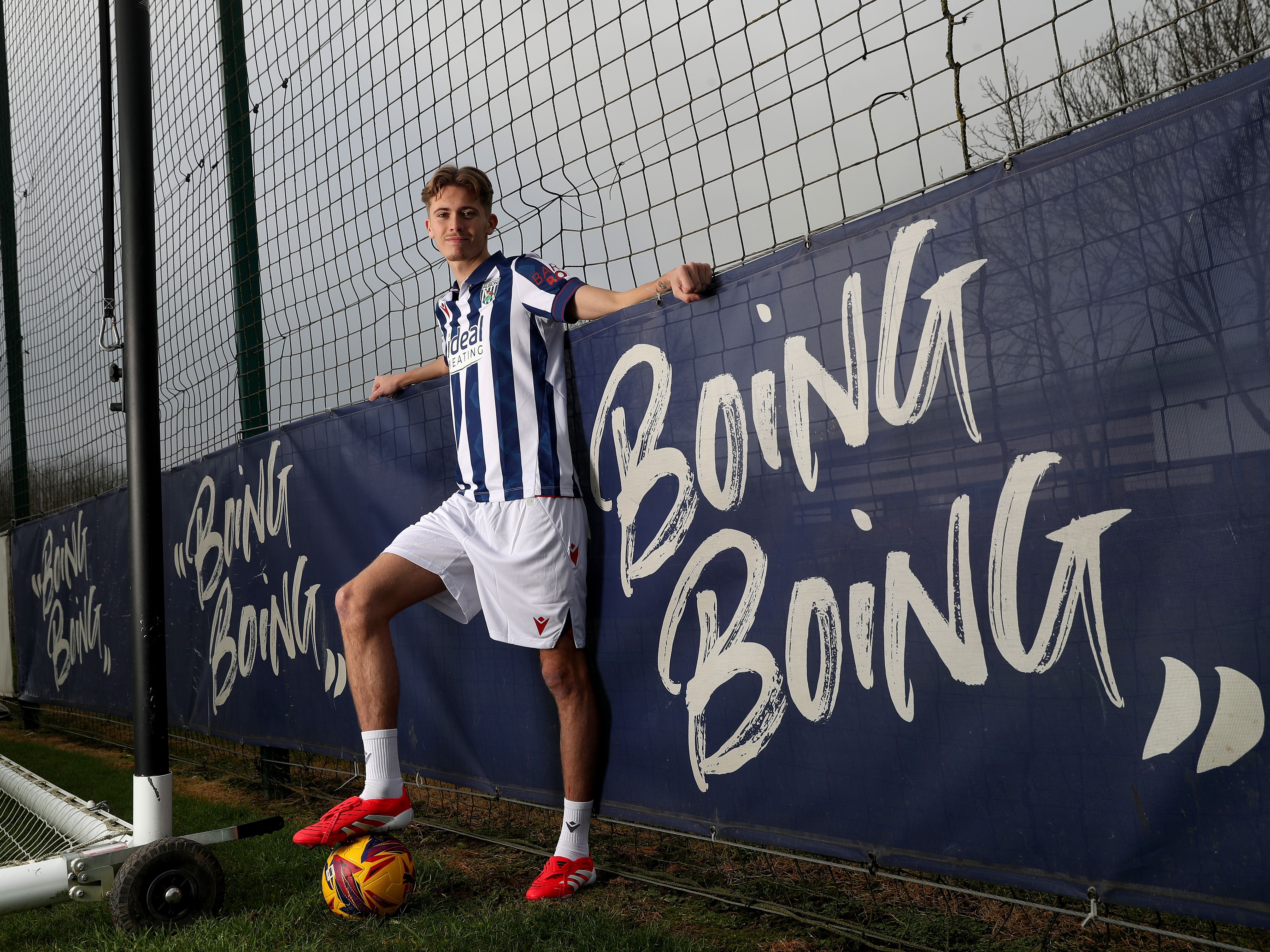 Isaac Price in home kit with one foot on a yellow ball next to a sign saying 'Boing Boing'