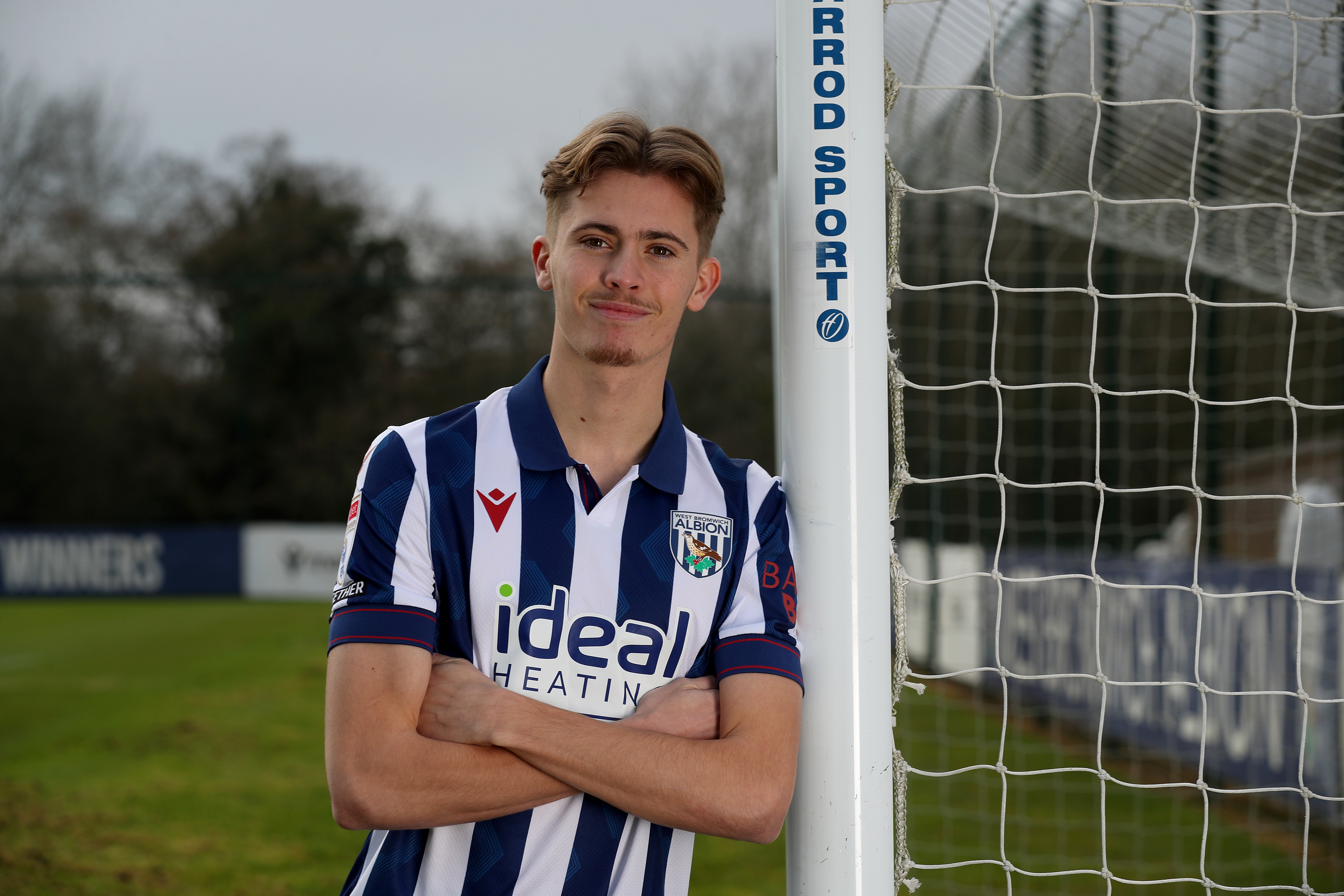 Isaac Price in a home shirt stood next to a goal post with his arms folded 