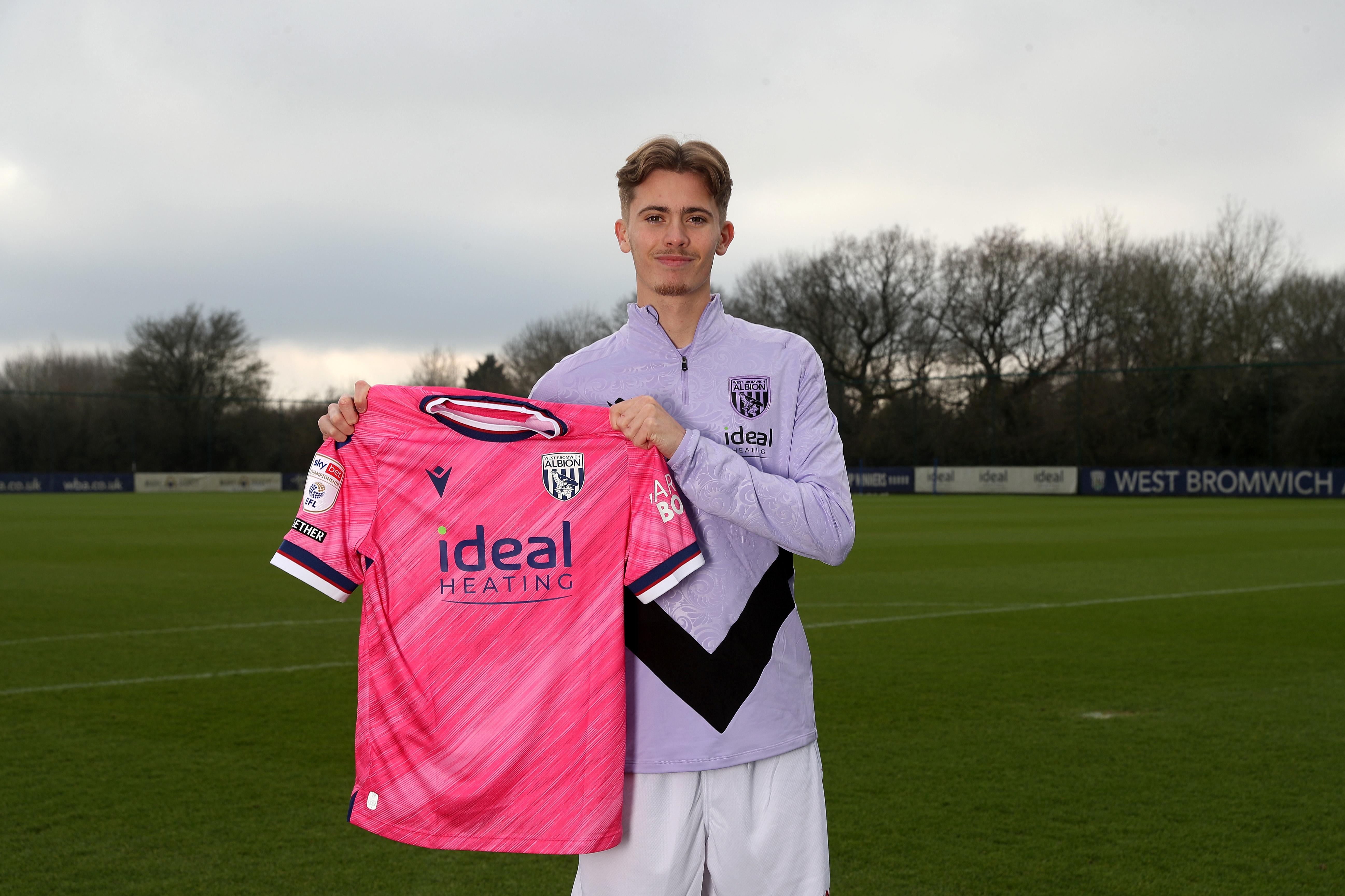 Isaac Price holding up a WBA pink away shirt 