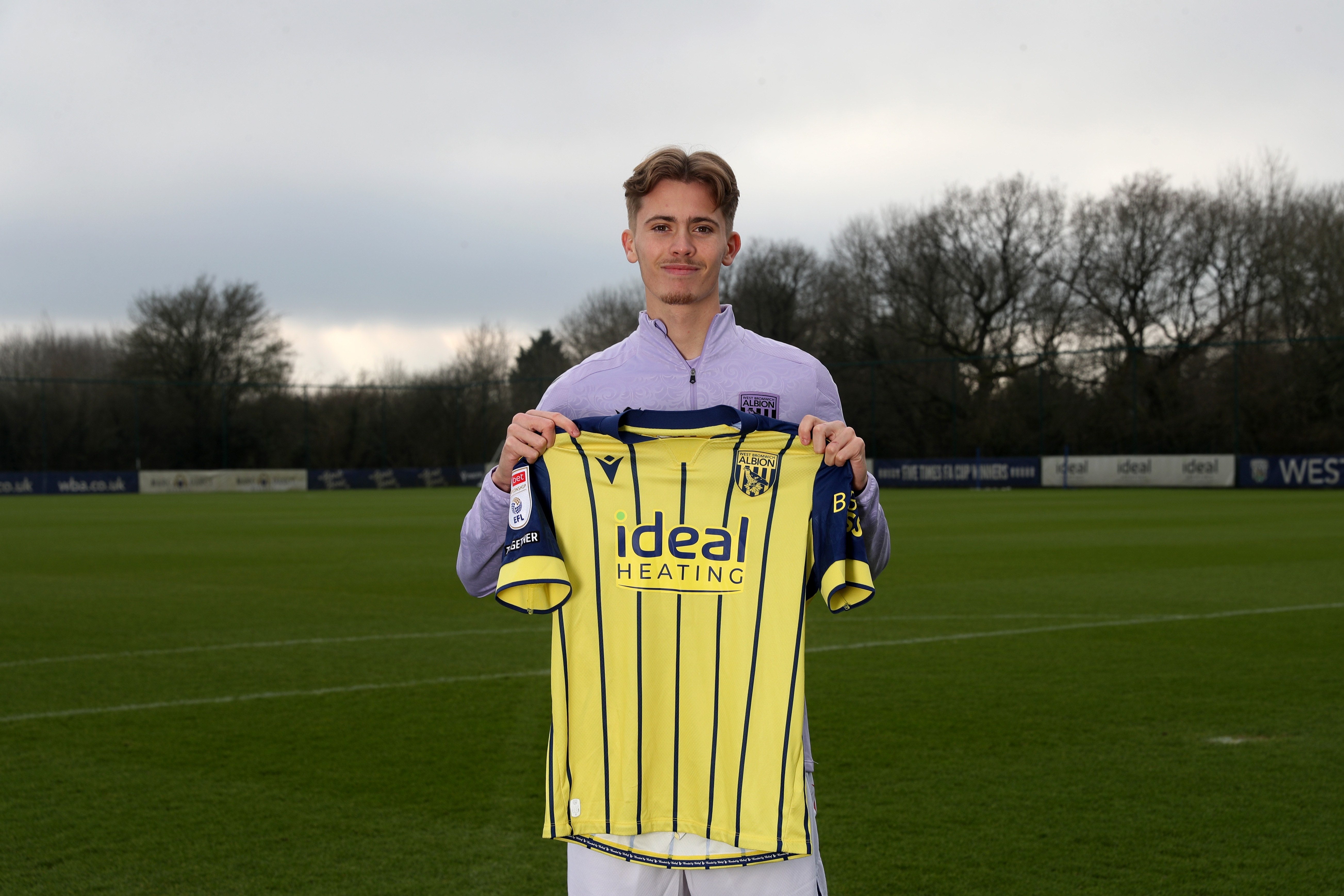 Isaac Price holding up a WBA yellow away shirt 