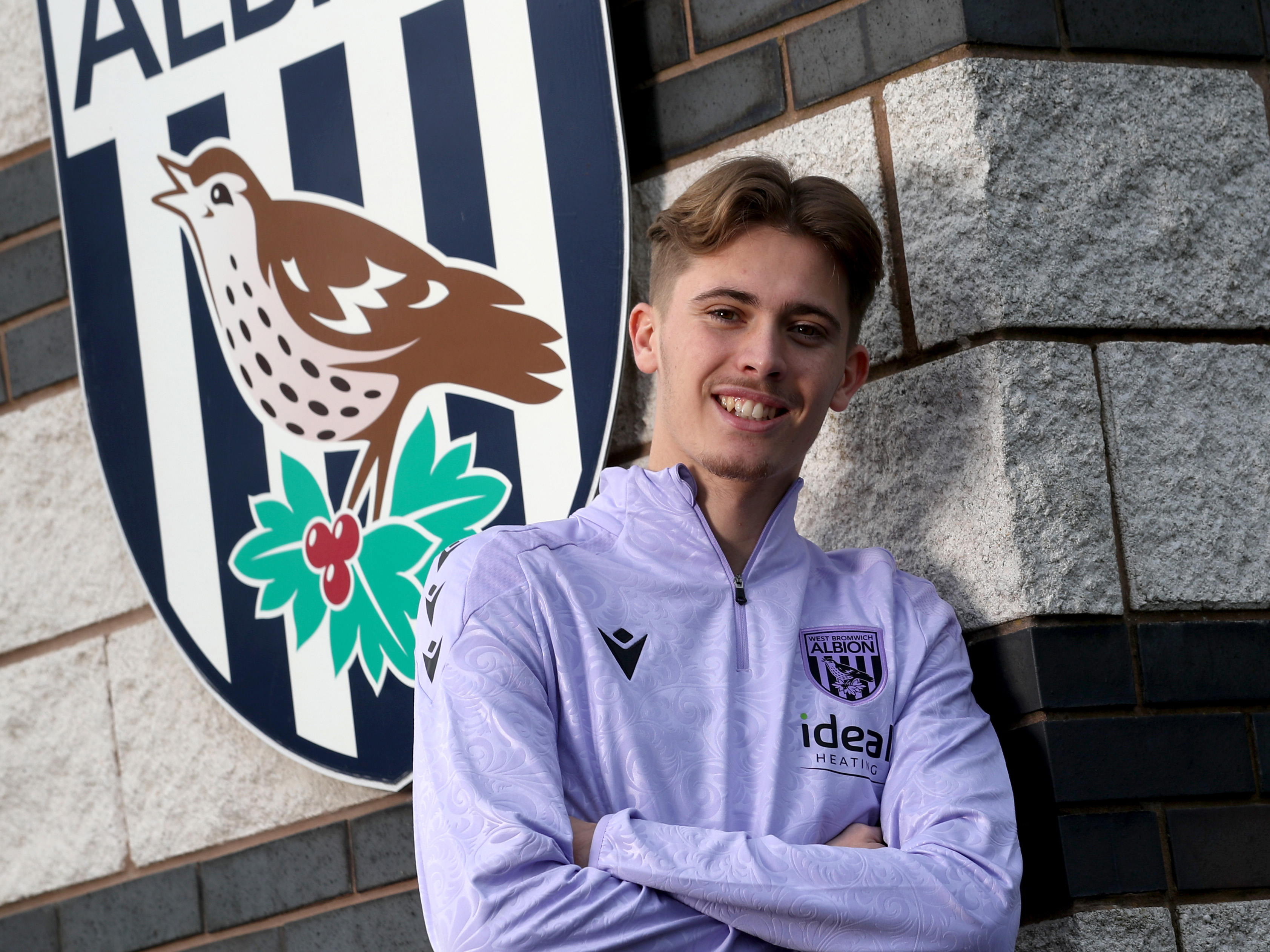 Isaac Price posing for a photo in front of a WBA badge with his arms folded 