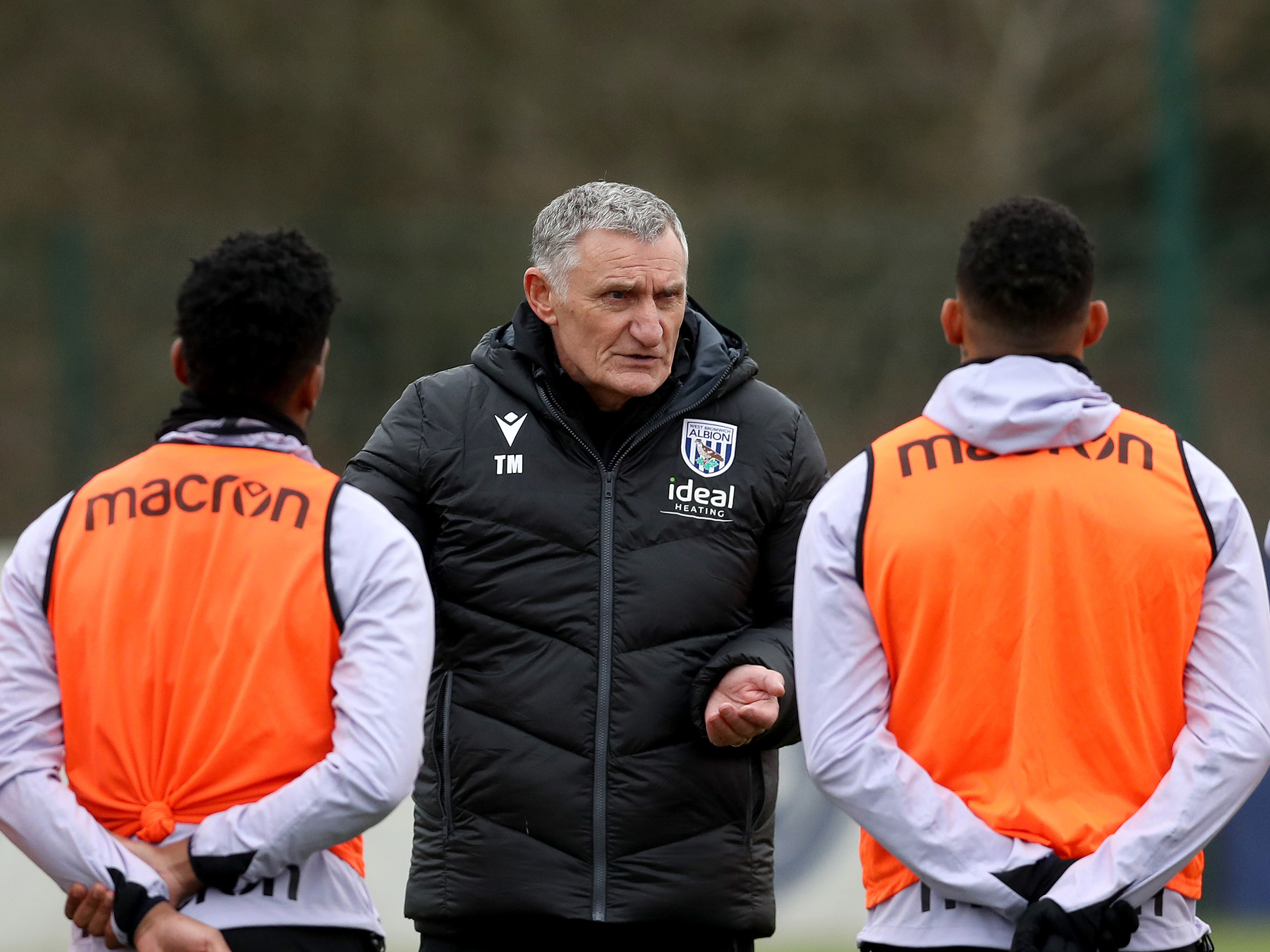 Tony Mowbray on the training pitch talking to two players in orange bibs 