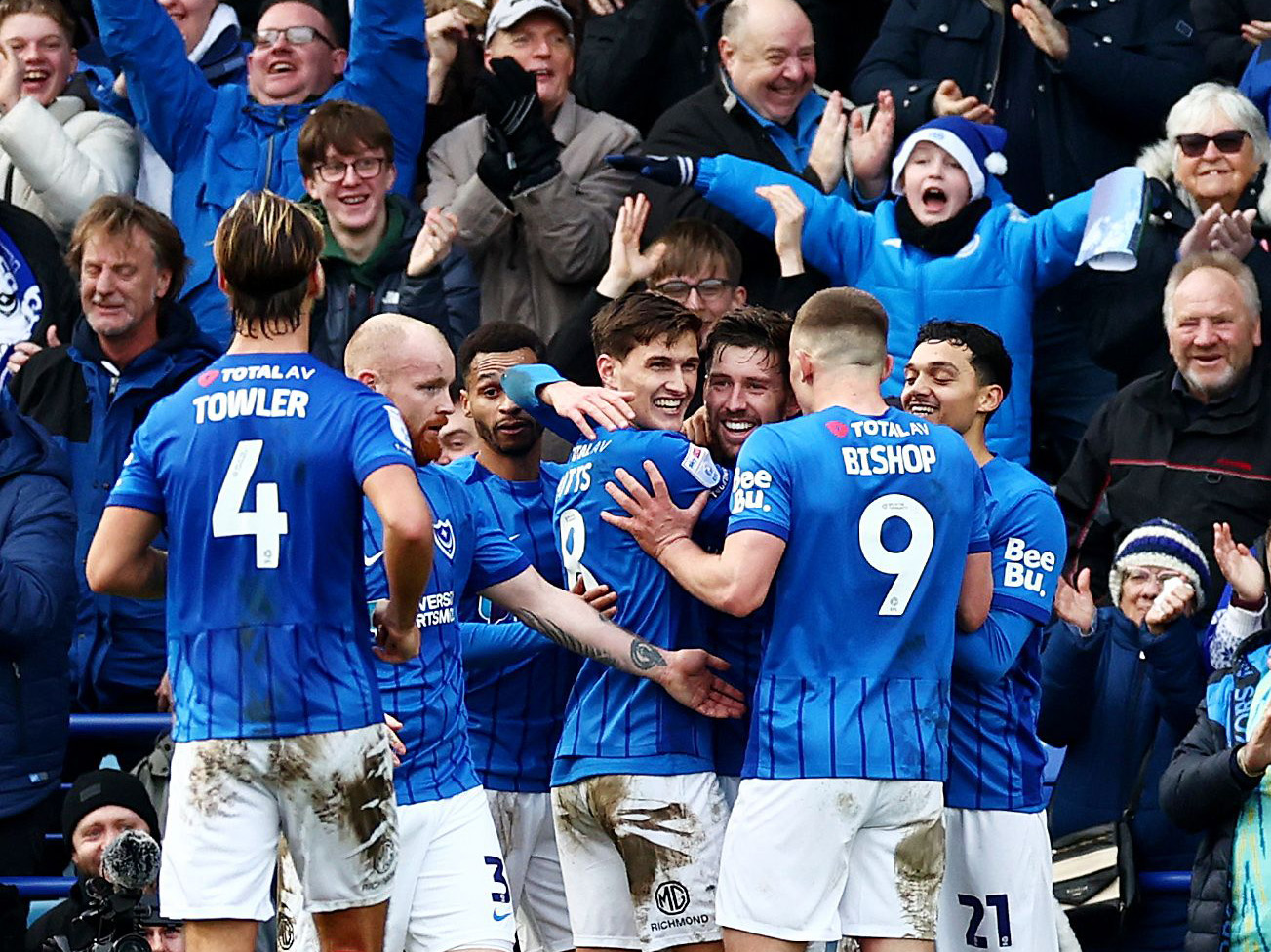 Several Portsmouth players in their home kit celebrate a goal in front of their fans 