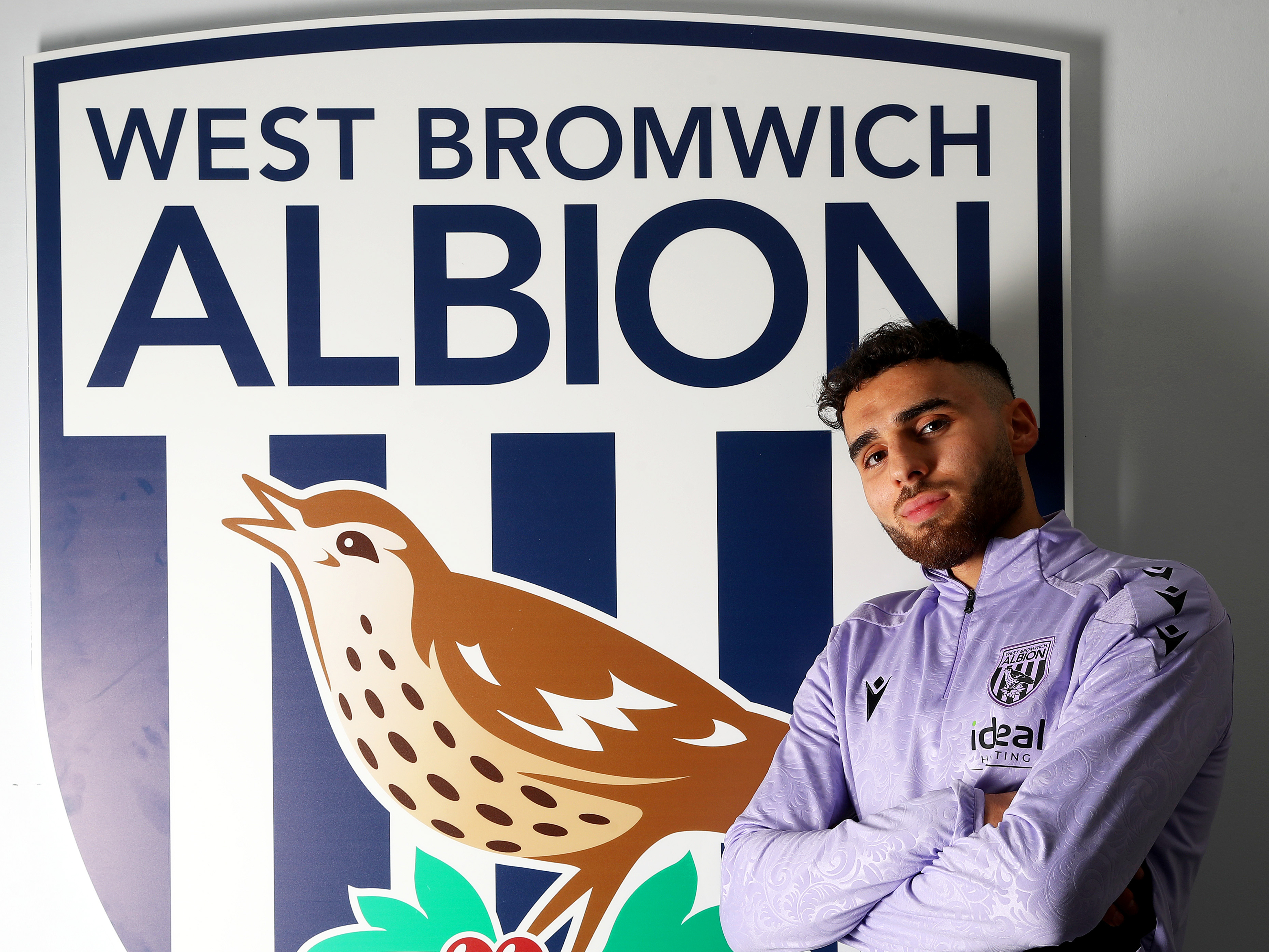 Tammer Bany posing for a photo in front of a big Albion badge with his arms crossed 