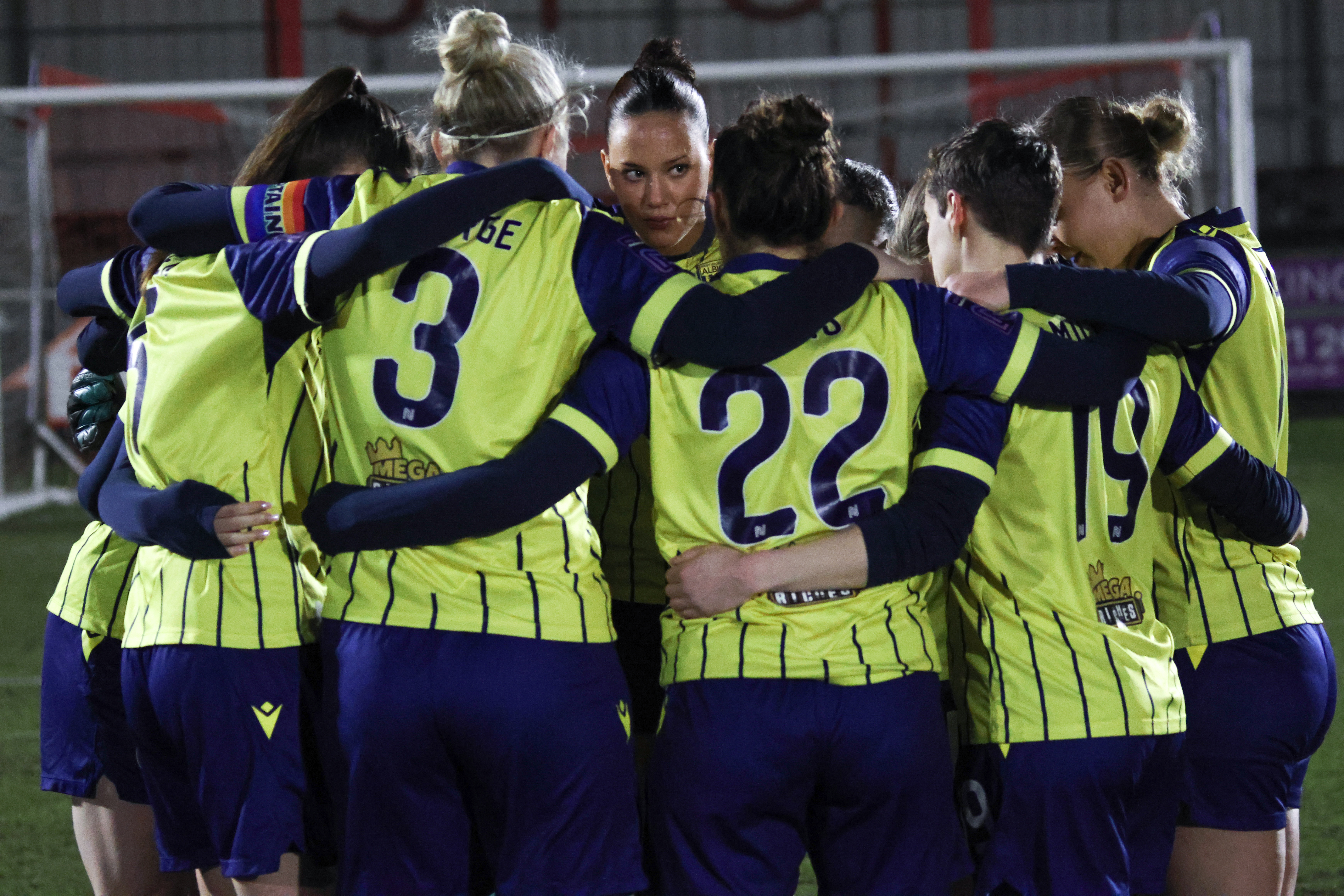 Albion Women in a team huddle in the yellow and navy blue away kit before a game