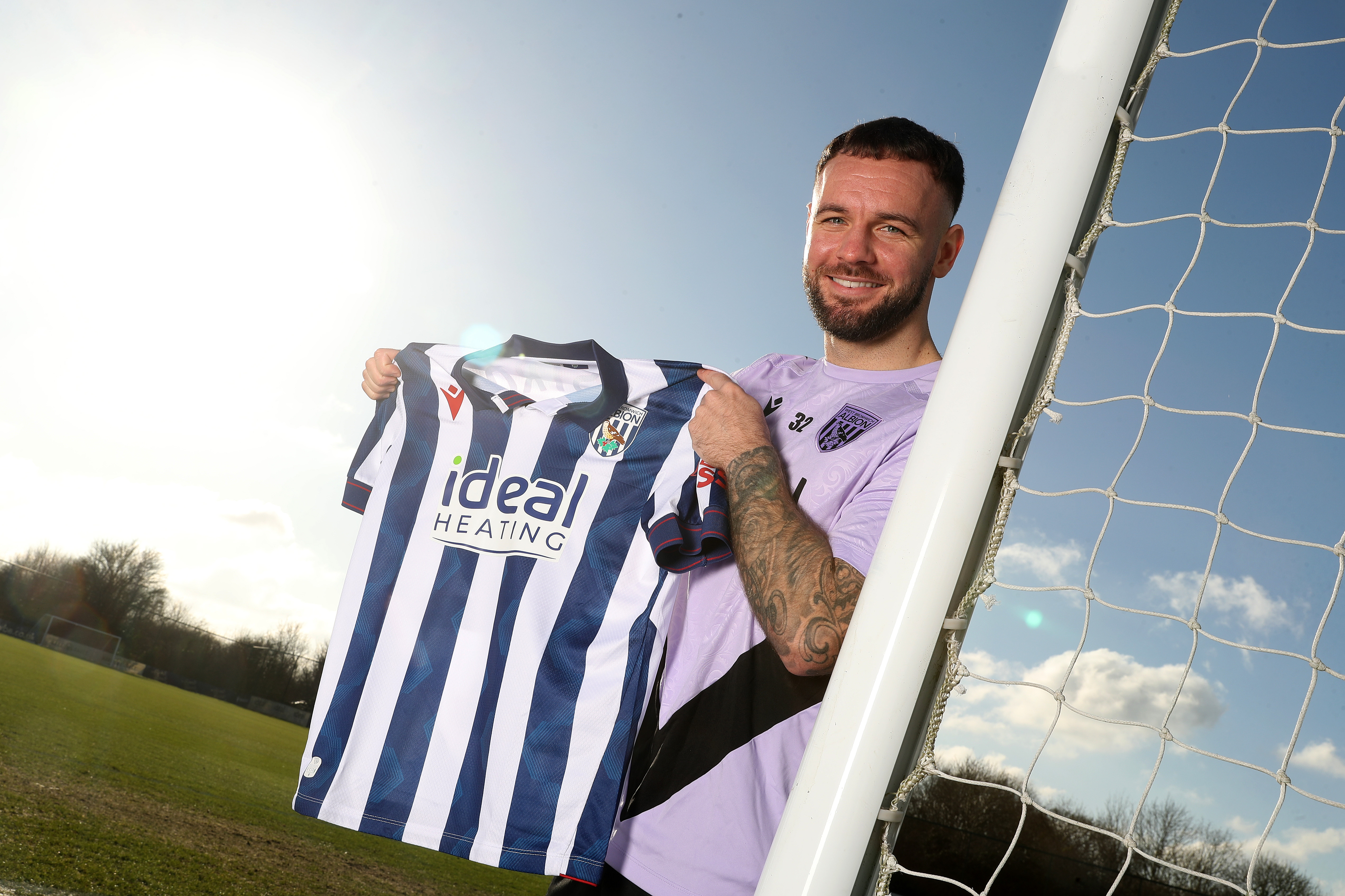 Adam Armstrong holding up a home shirt while leaning on a goal post