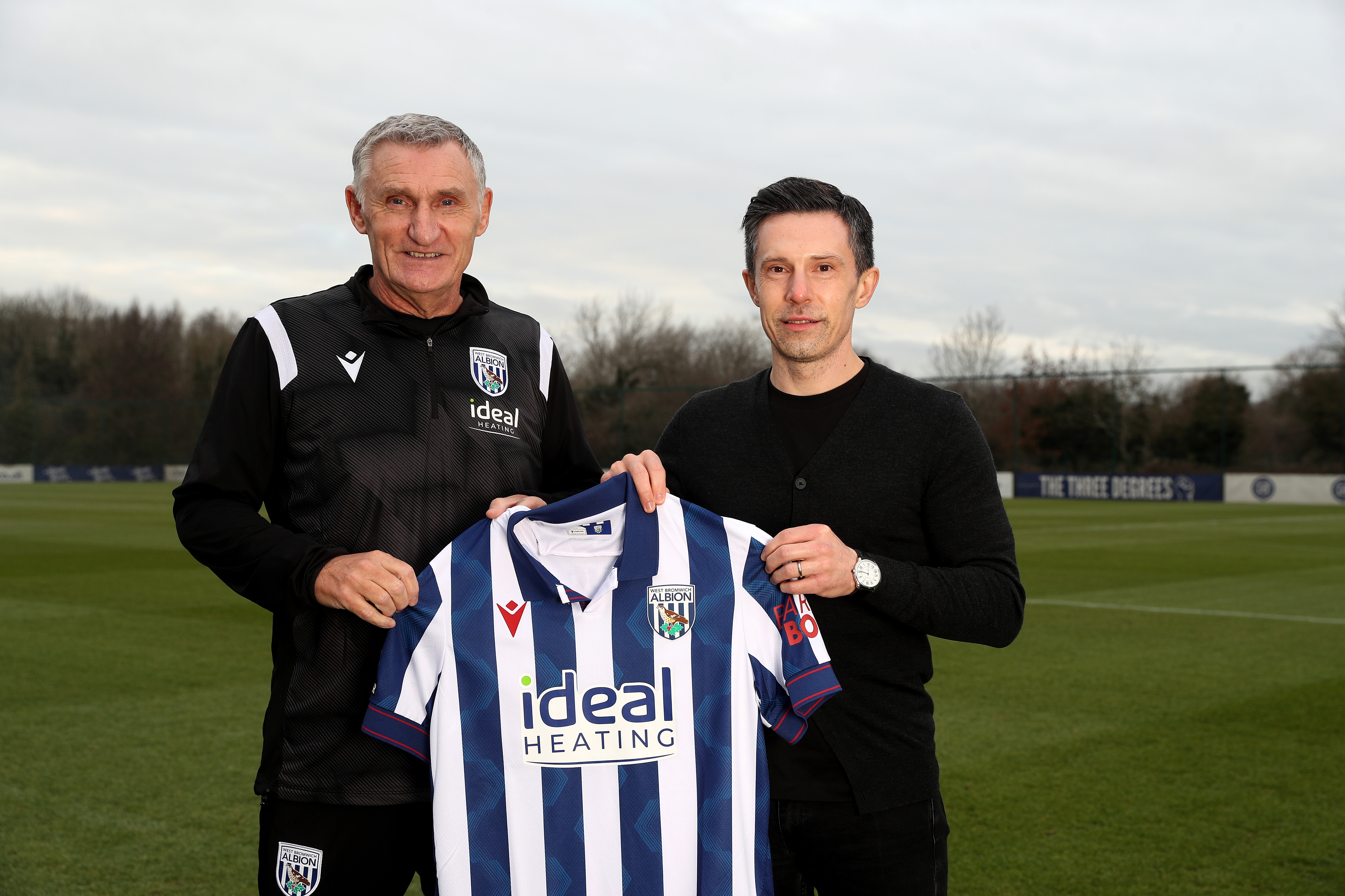 Tony Mowbray and Andrew Nestor smiling at the camera while holding a home shirt out on a training pitch 