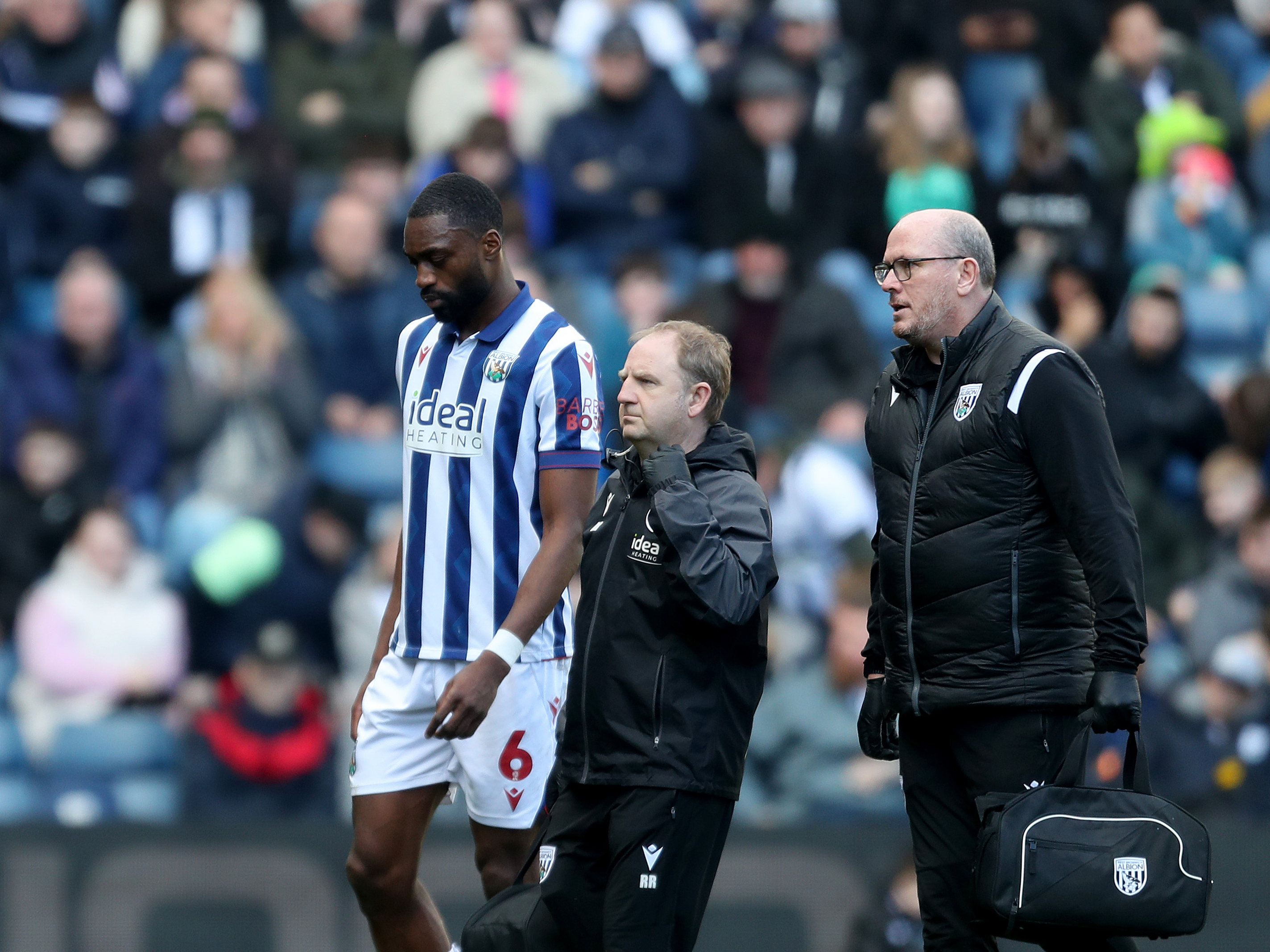 Semi Ajayi leaves the pitch at The Hawthorns wearing the home kit with two club physios 