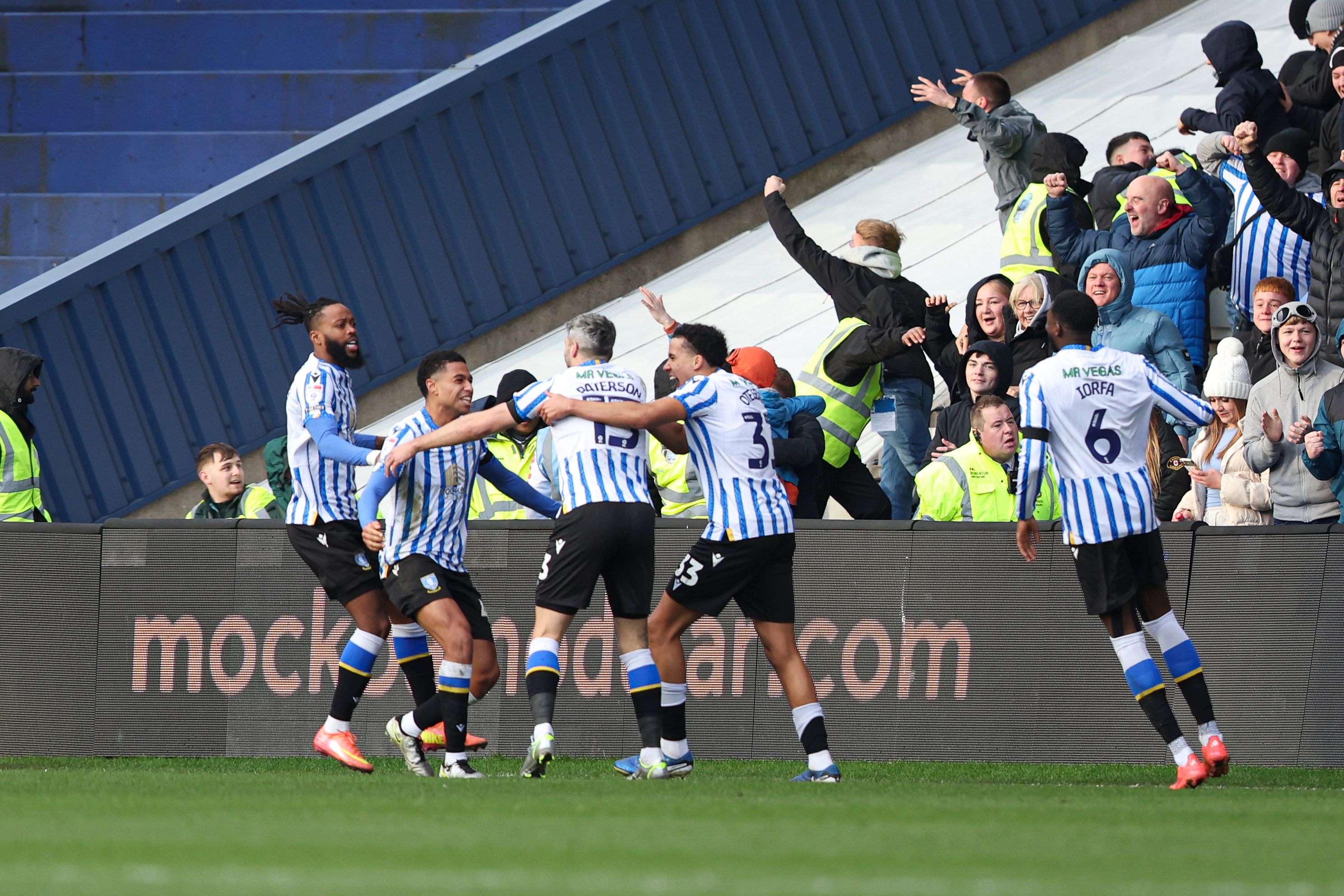 Several Sheffield Wednesday players celebrating a goal scoring in their home kit with supporters in the background 