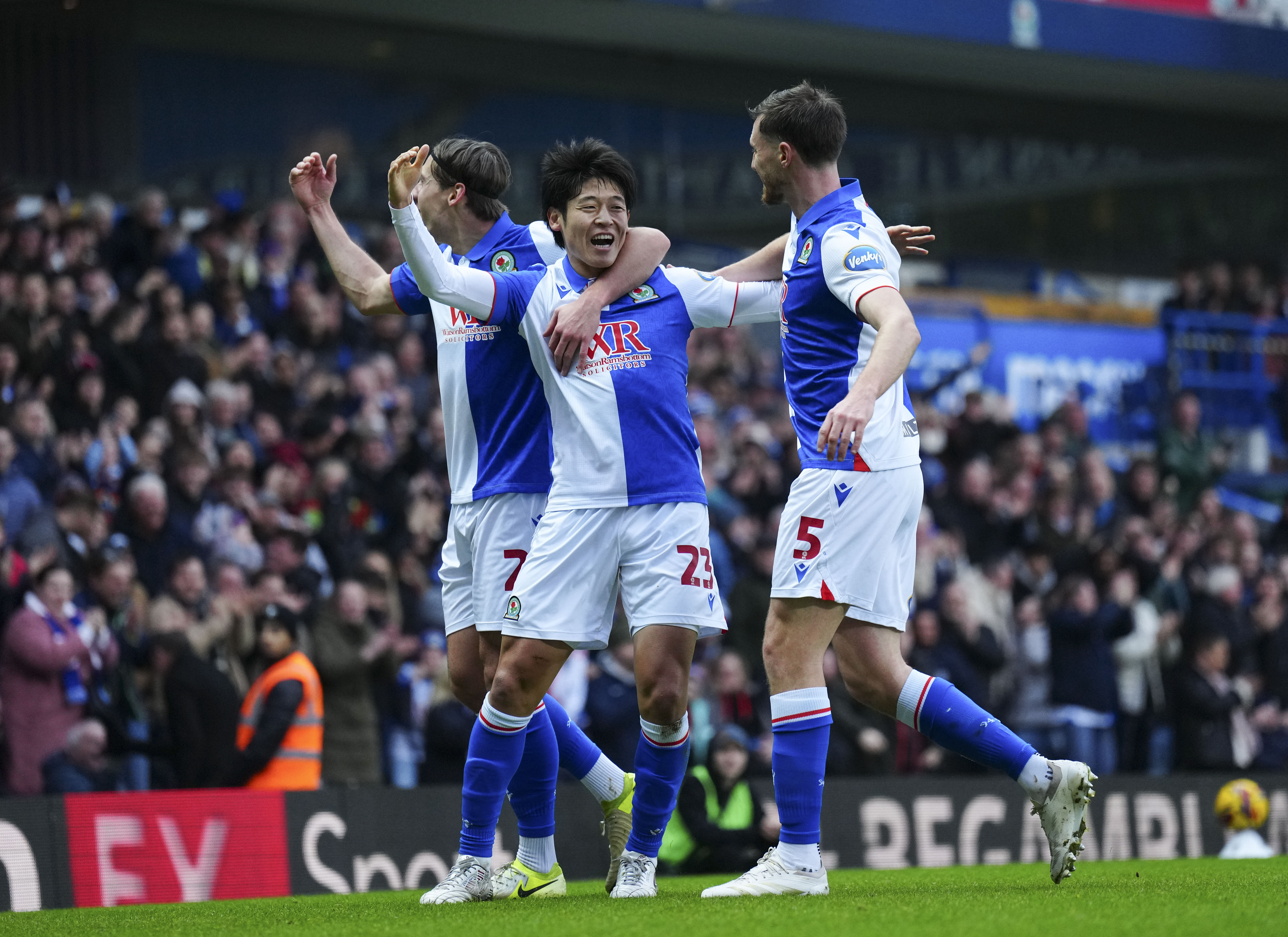 Three Blackburn Rovers players celebrate a goal scored in their home kit