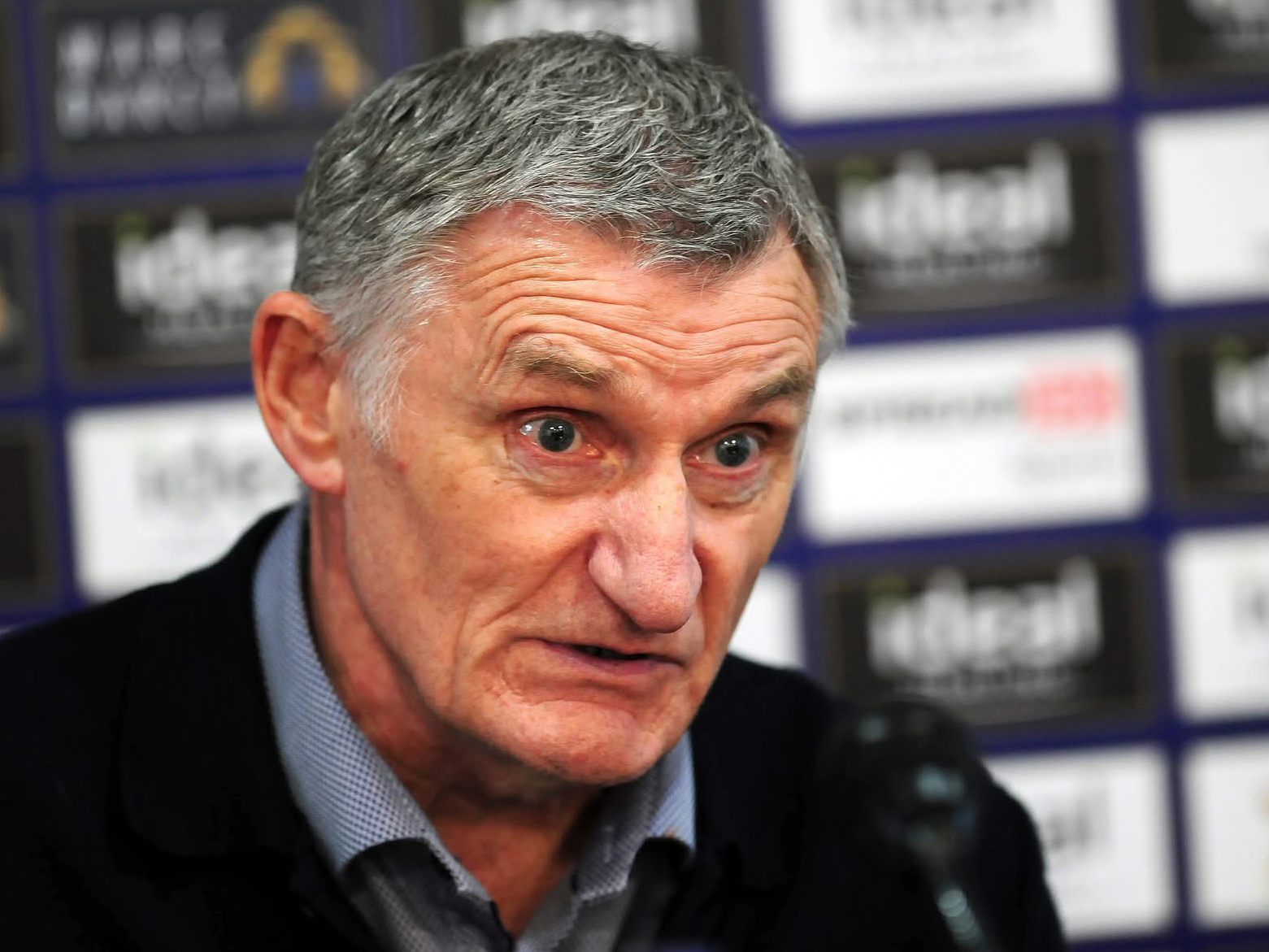 Tony Mowbray speaking at a press conference in front of a sponsor board 