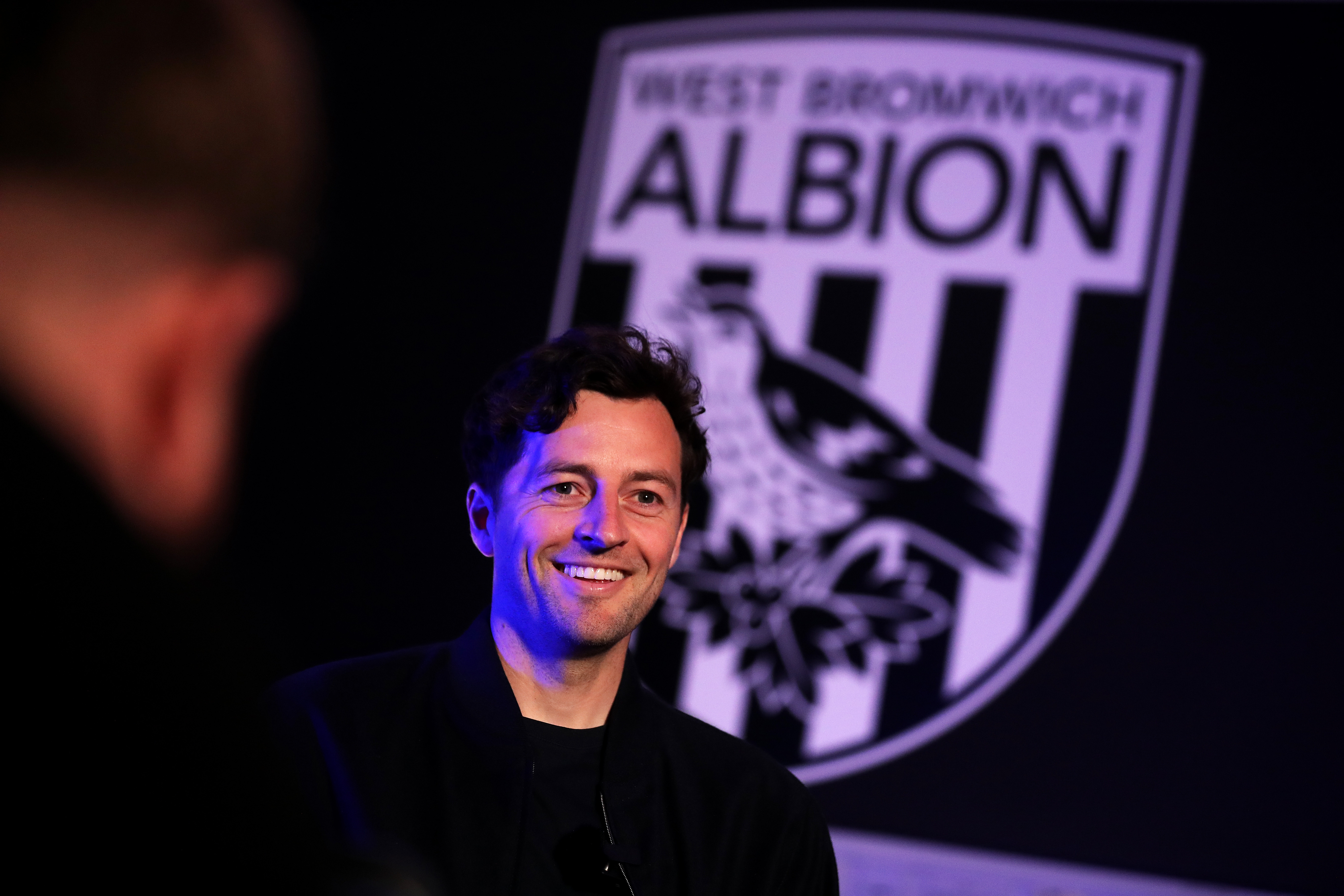 Ryan Mason smiling while sat in front of a big WBA badge