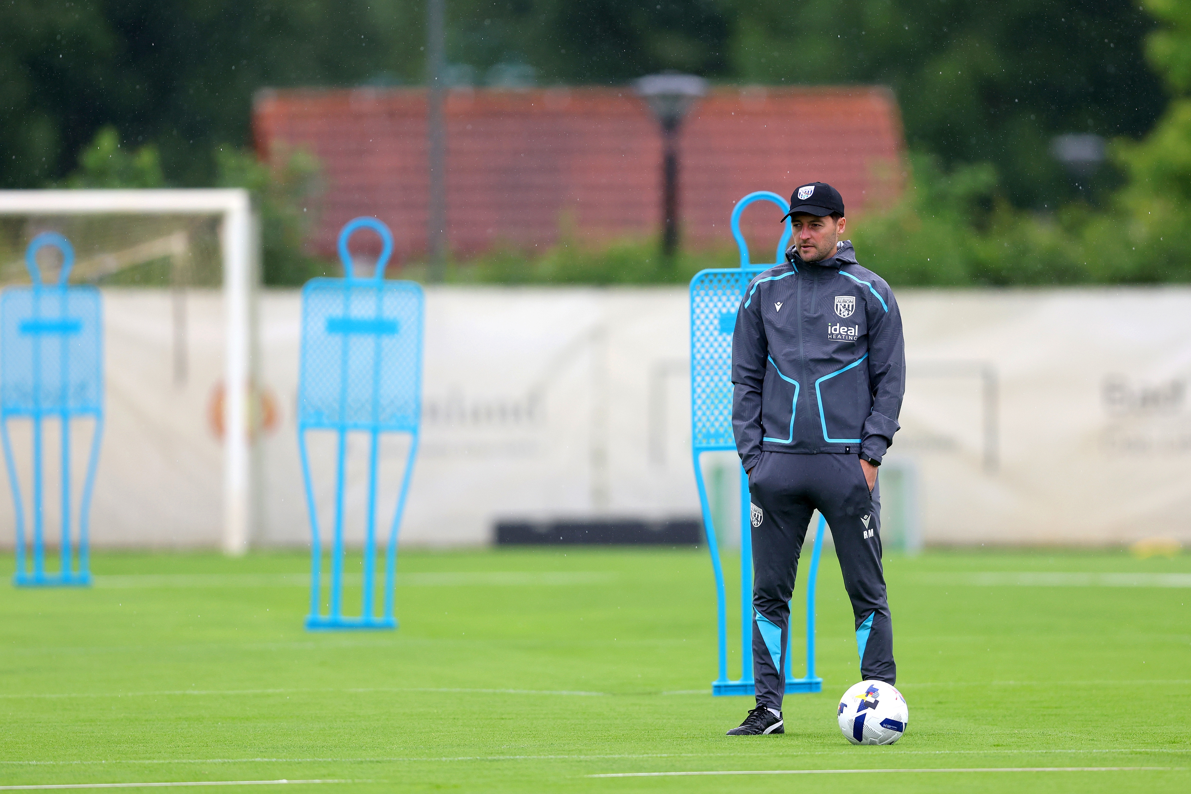 Ryan Mason watching training in the rain stood next to a mannequin in a cap
