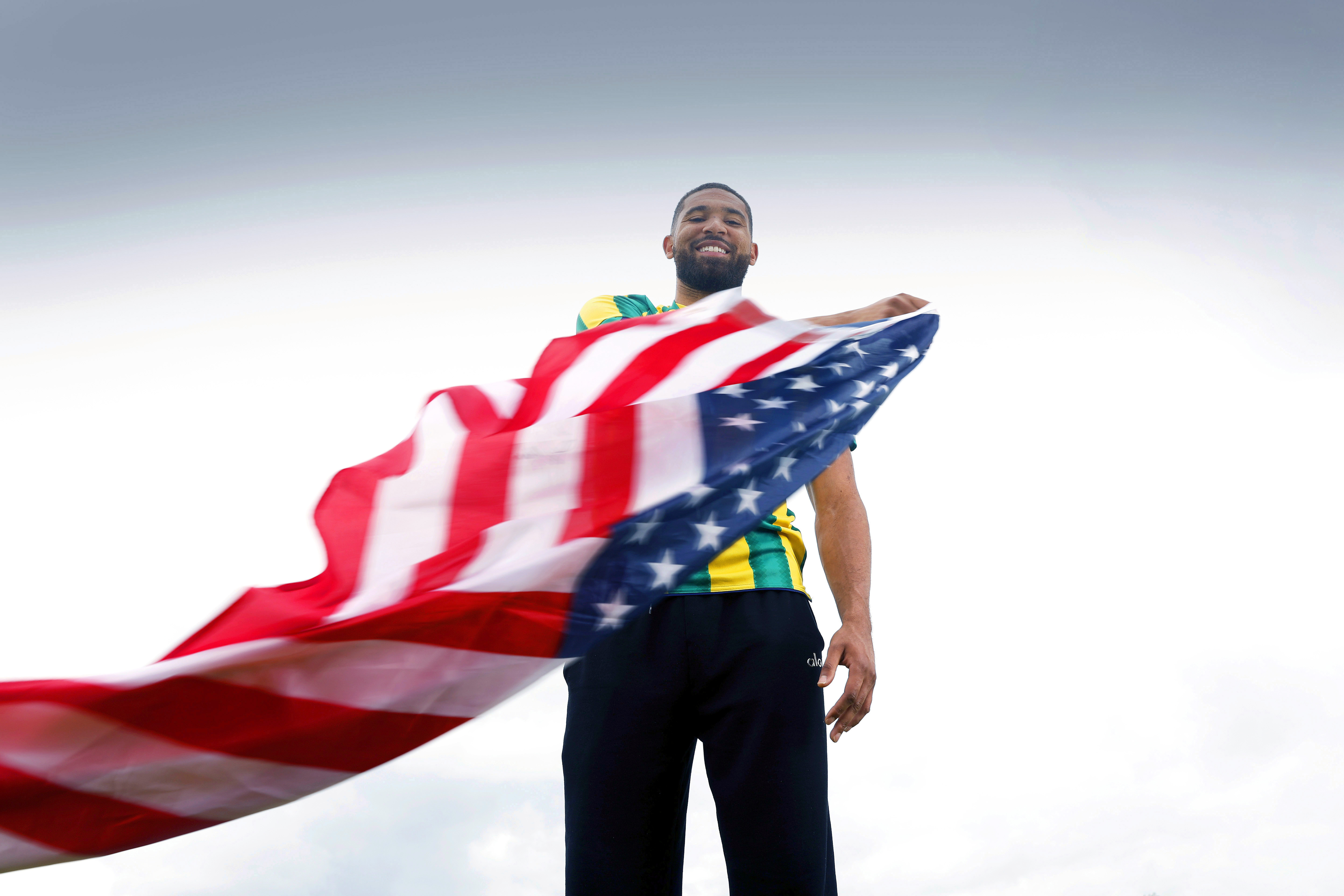 George Campbell smiling while stood in an away WBA shirt waving an American flag