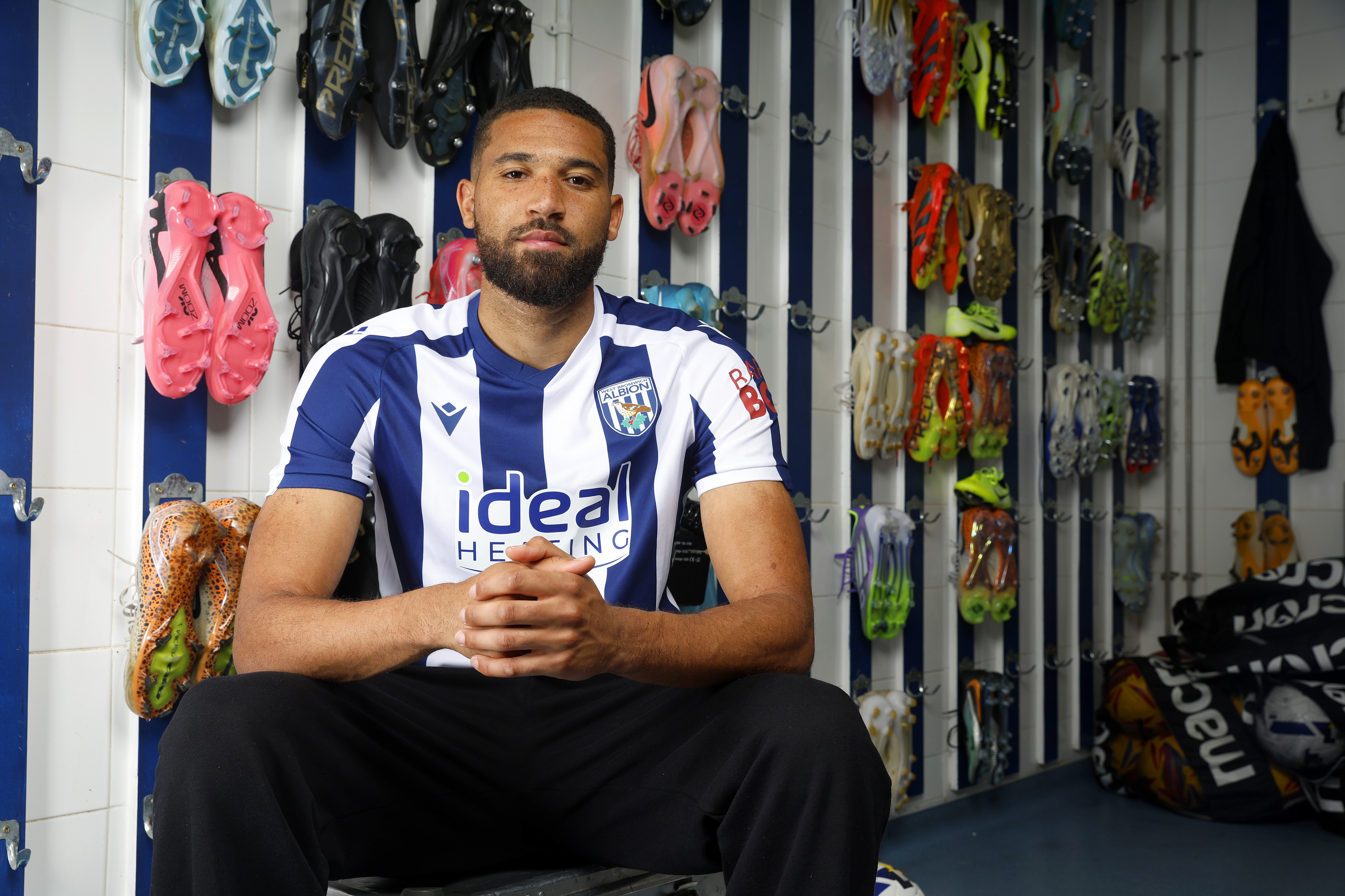 George Campbell sat in the boot room in a home WBA shirt smiling at the camera 