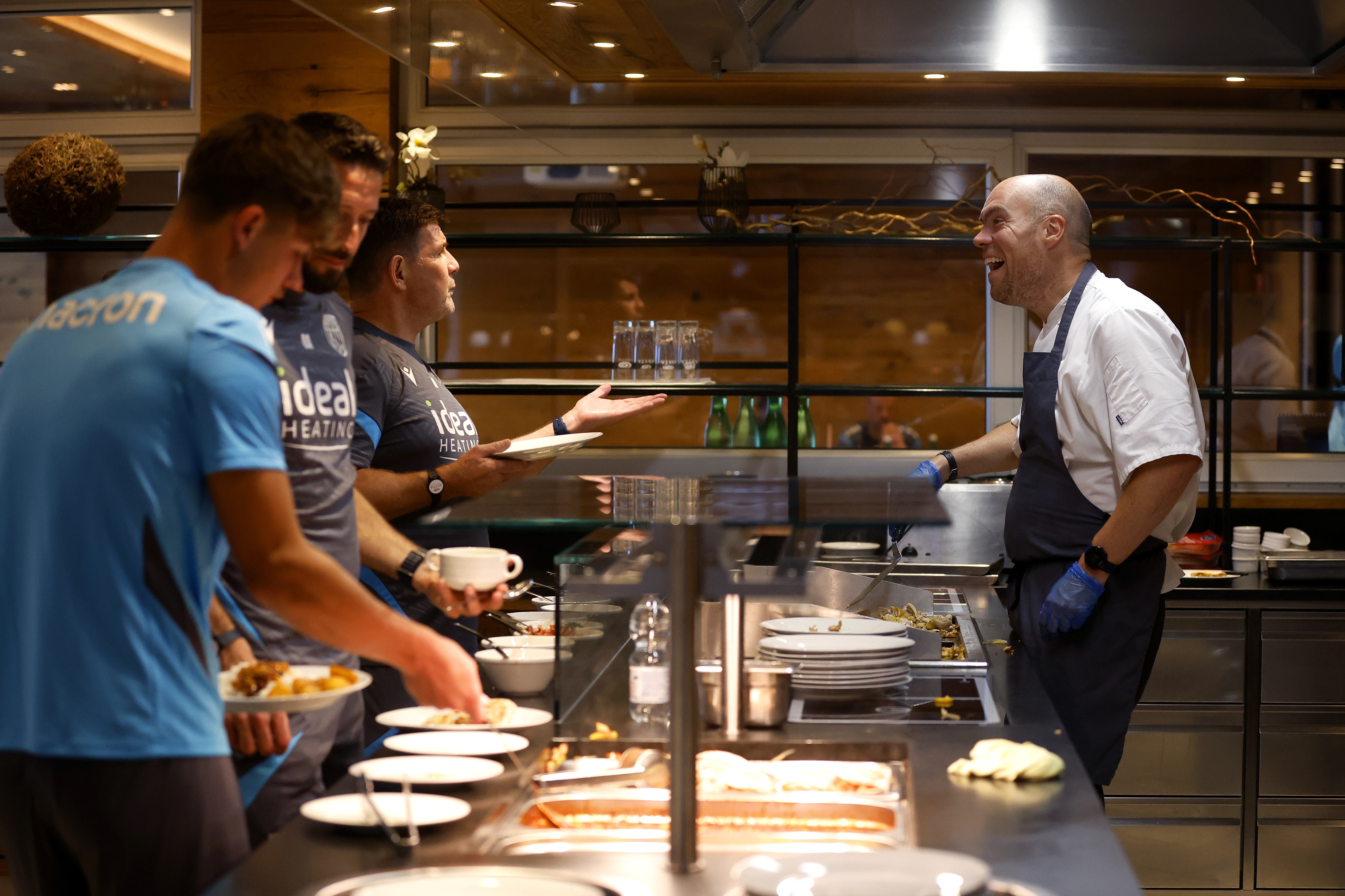 A WBA chef laughing with players and staff in the kitchen at the hotel