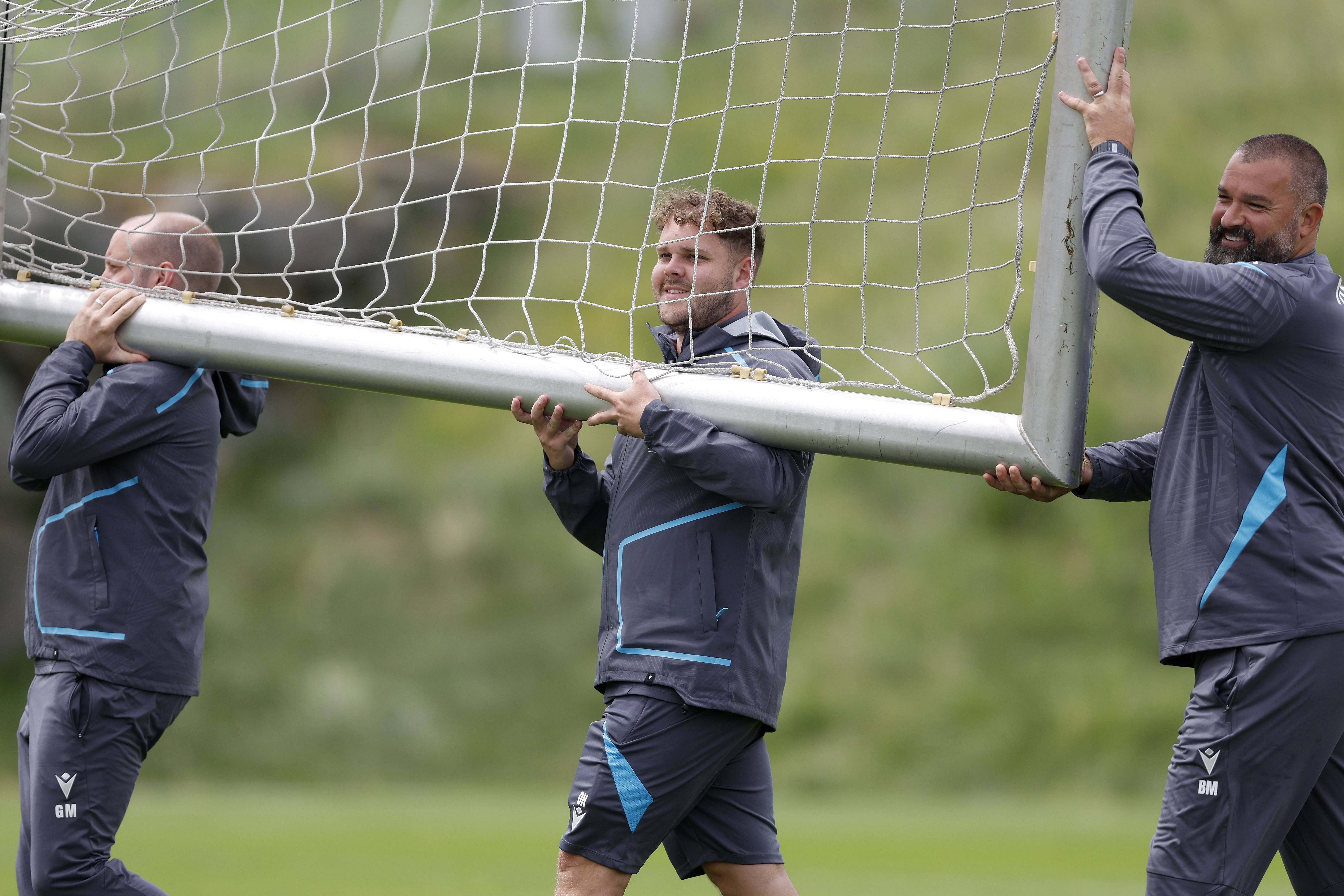 Three Albion staff members carrying a goal on a training pitch 