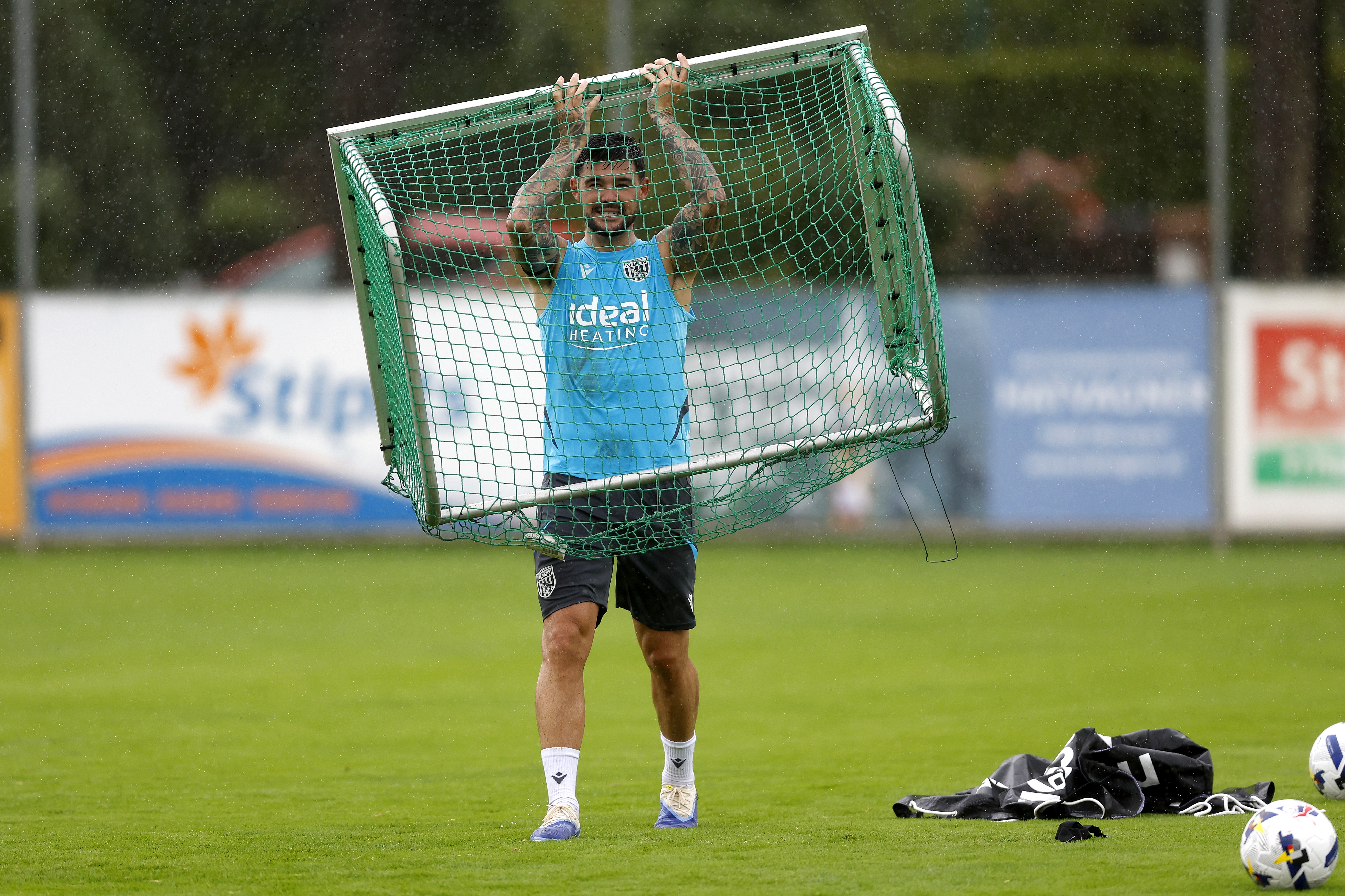 Alex Mowatt holding up a mini goal above his head during a training session in the rain