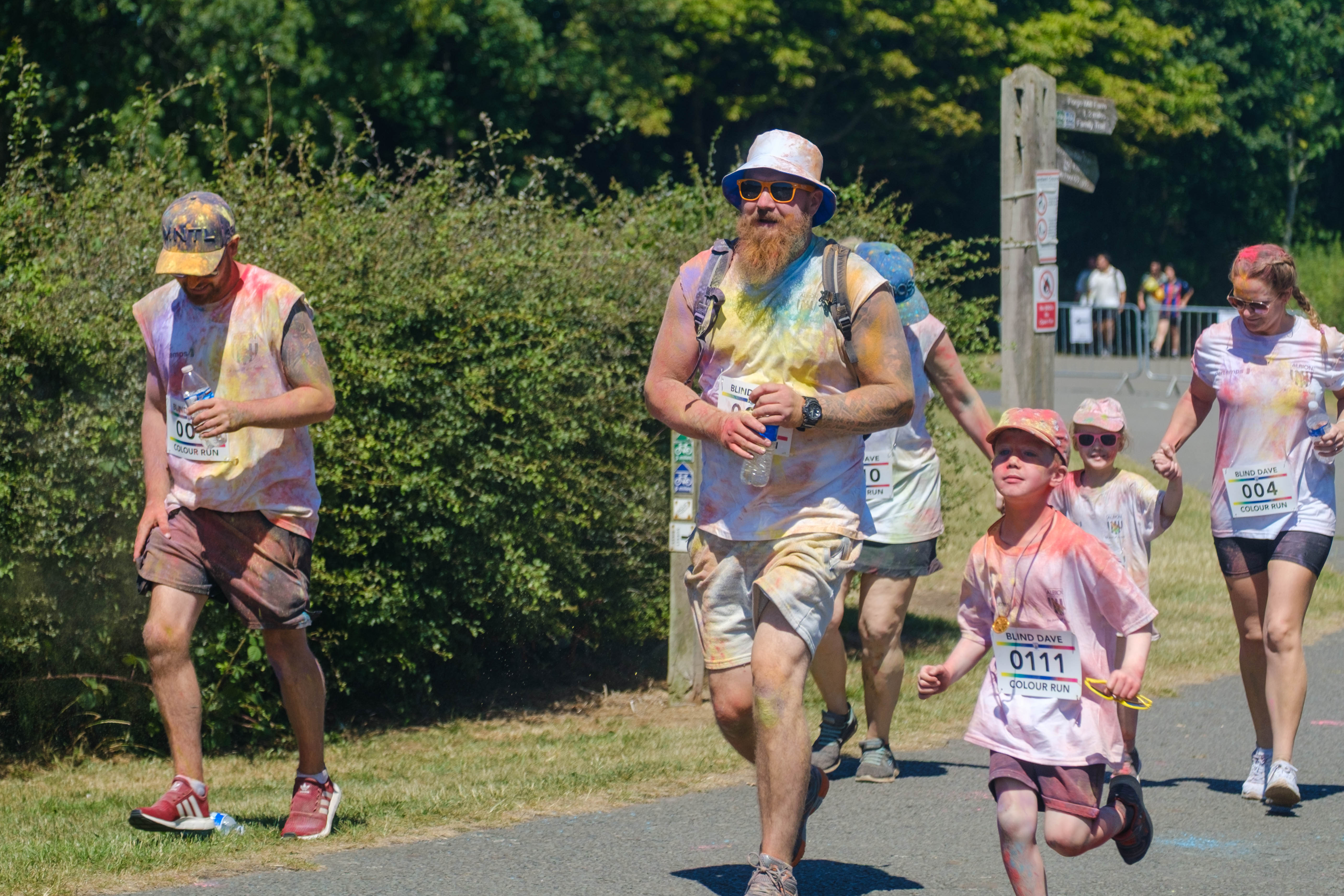 More runners smiling and covered in paint, heading towards the finish line.