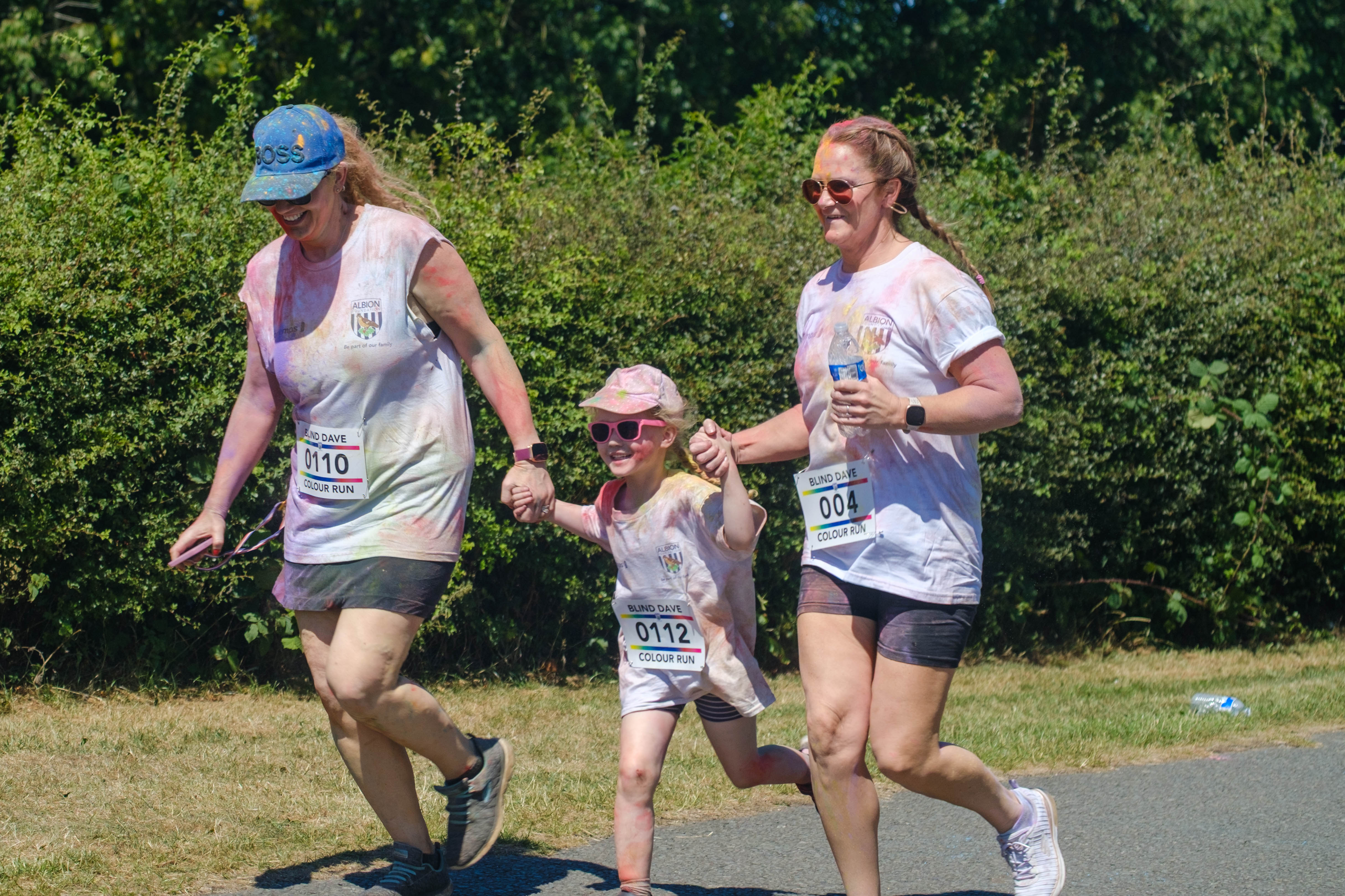 Two woman and a child holding hands heading towards the finish line.