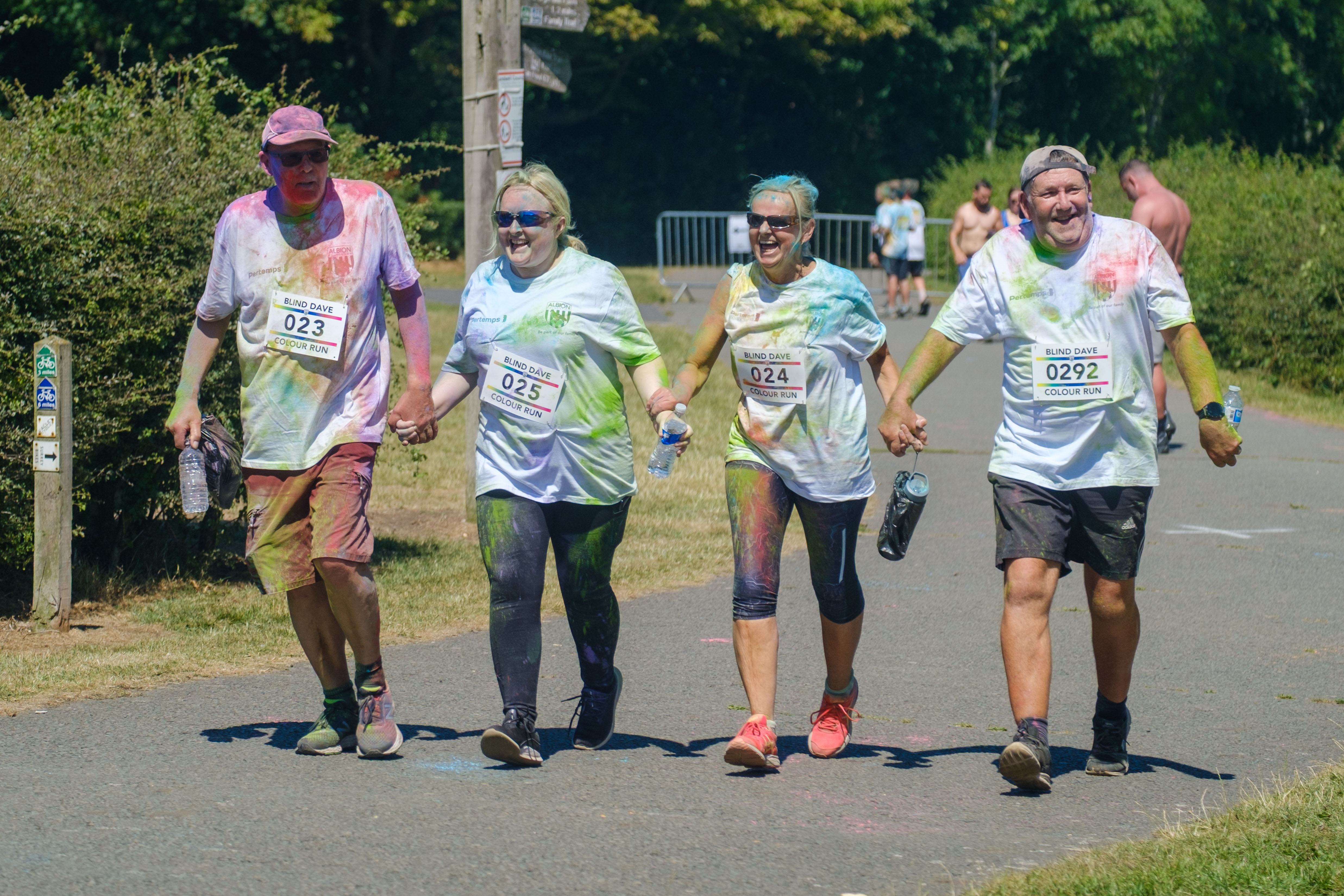 Four adult participants holding hands heading towards the finish line.